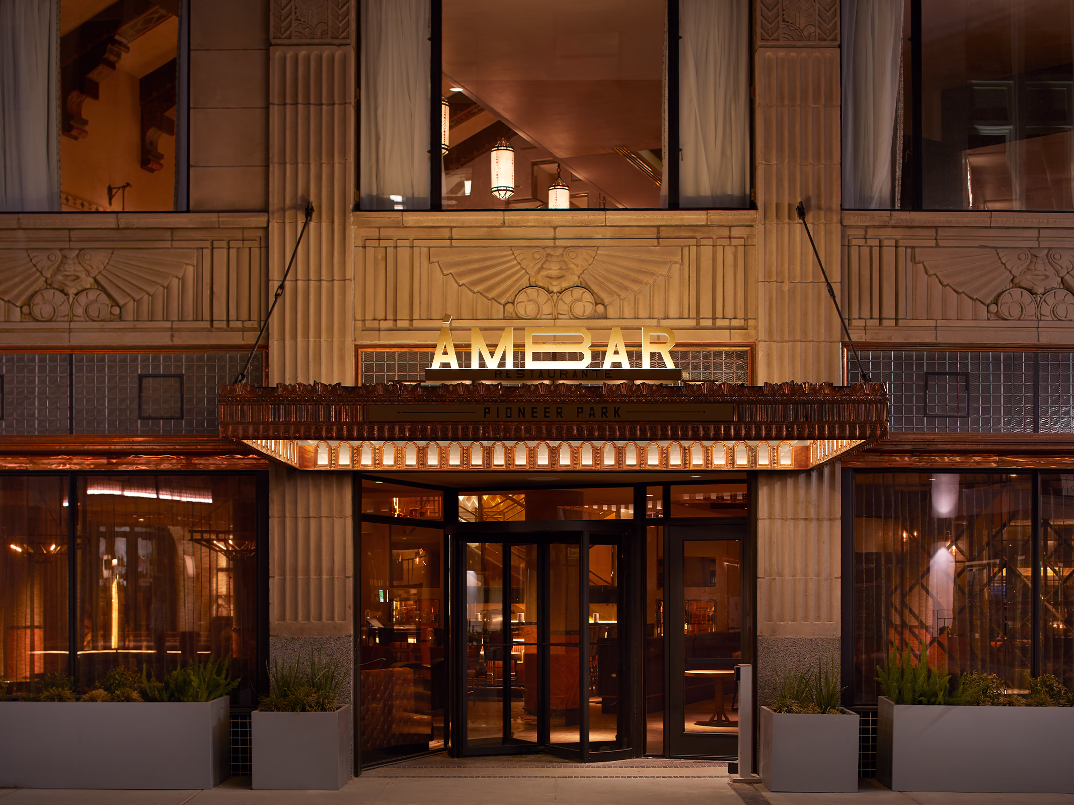 Full facade view of Ámbar Restaurante at Plaza Hotel Pioneer Park, showing the illuminated marquee, revolving door entrance, and upper-floor windows.