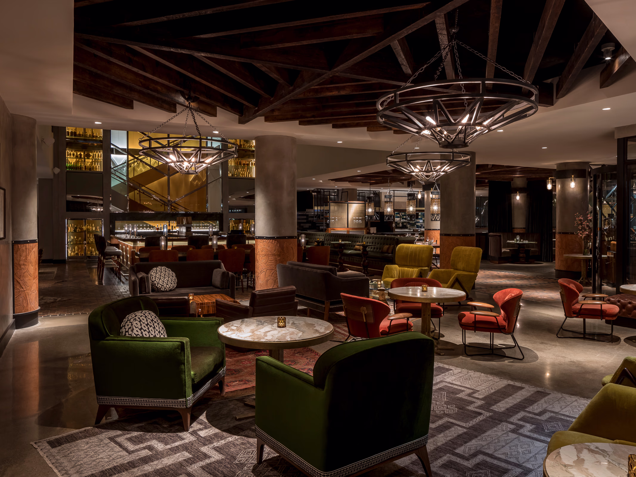Jewel-tone velvet chairs and marble cocktail tables in Ámbar Restaurante's lounge, with hand-tooled leather columns and iron chandeliers overhead.