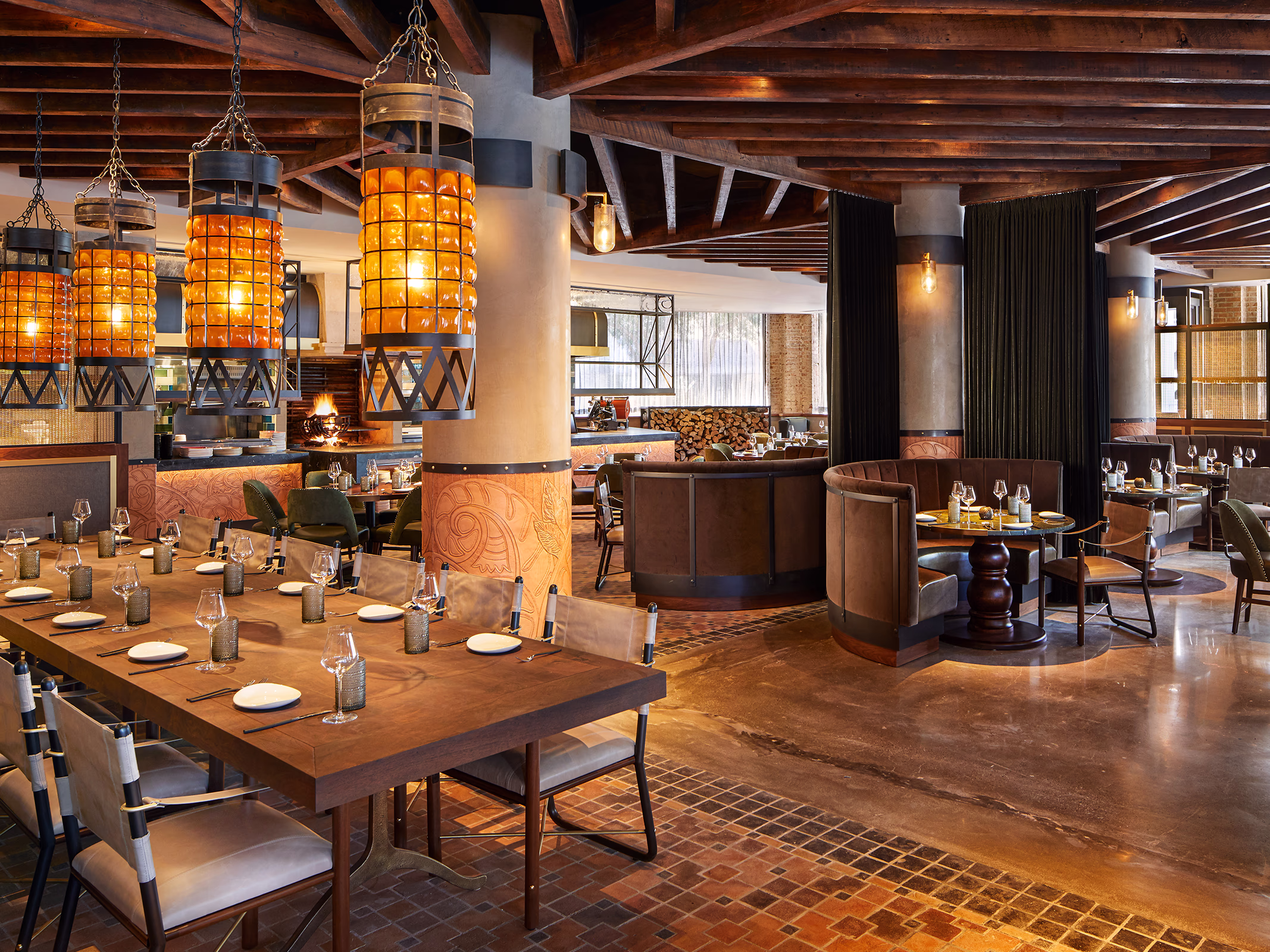 View toward Ámbar Restaurante's open kitchen and wood-fire grill, past a tooled leather column and curved leather booth seating.
