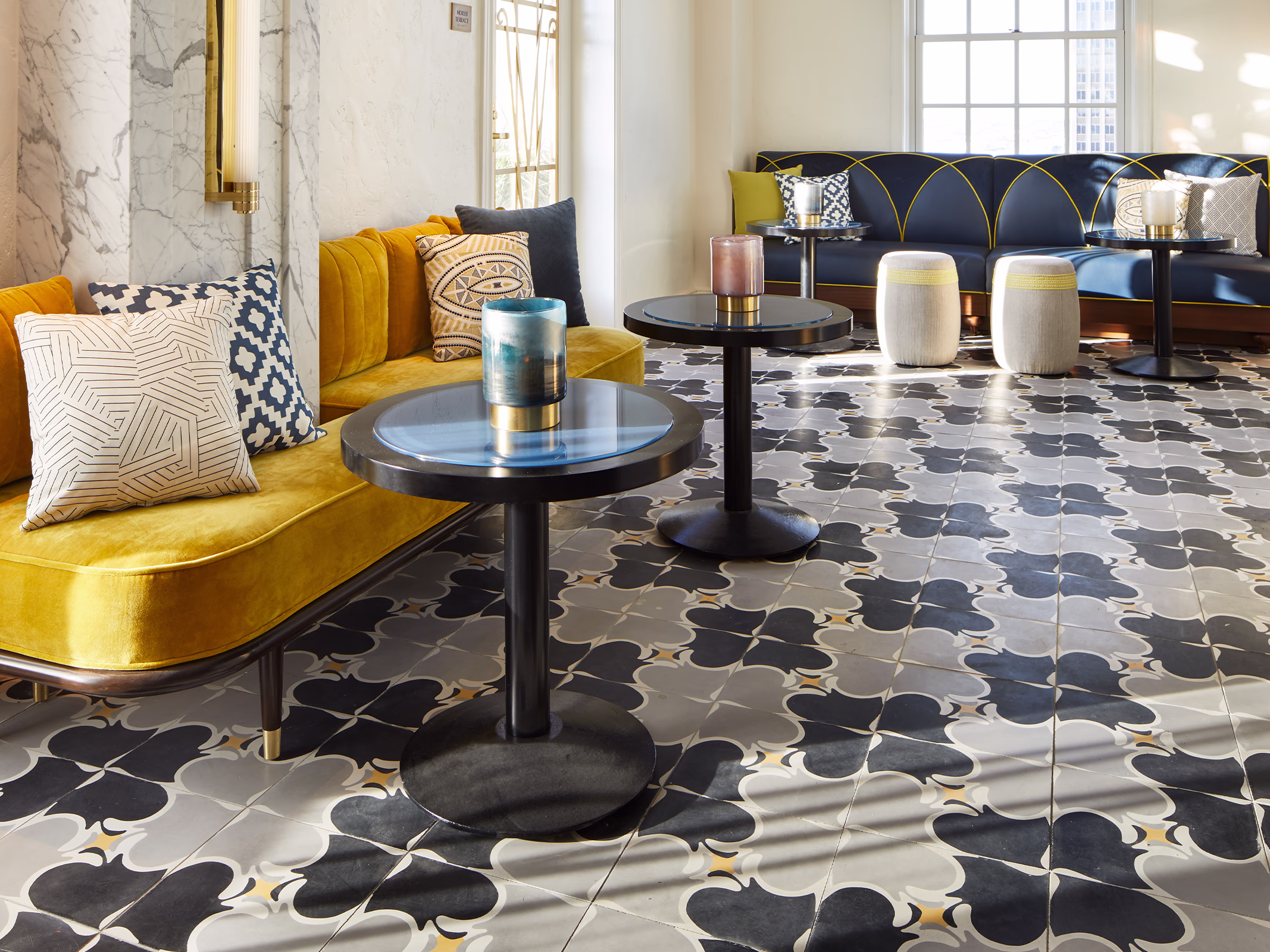 Interior lounge at La Perla in El Paso with patterned black and white cement tile flooring, a mustard velvet sofa, navy arched booth seating, and marble walls.
