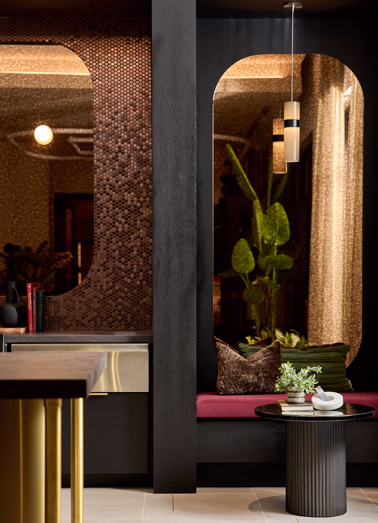 A dramatic bar and lounge nook at Modera SoBro featuring bronze penny tile walls, arched alcoves, a raspberry velvet bench, and a fluted black side table under moody ambient lighting.