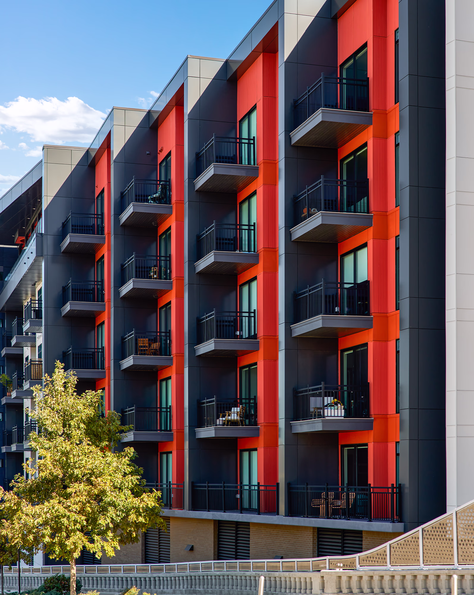 Close-up exterior view of Modera SoBro's upper floors, highlighting bold red vertical facade panels, dark charcoal cladding, and black metal balconies against a blue sky.