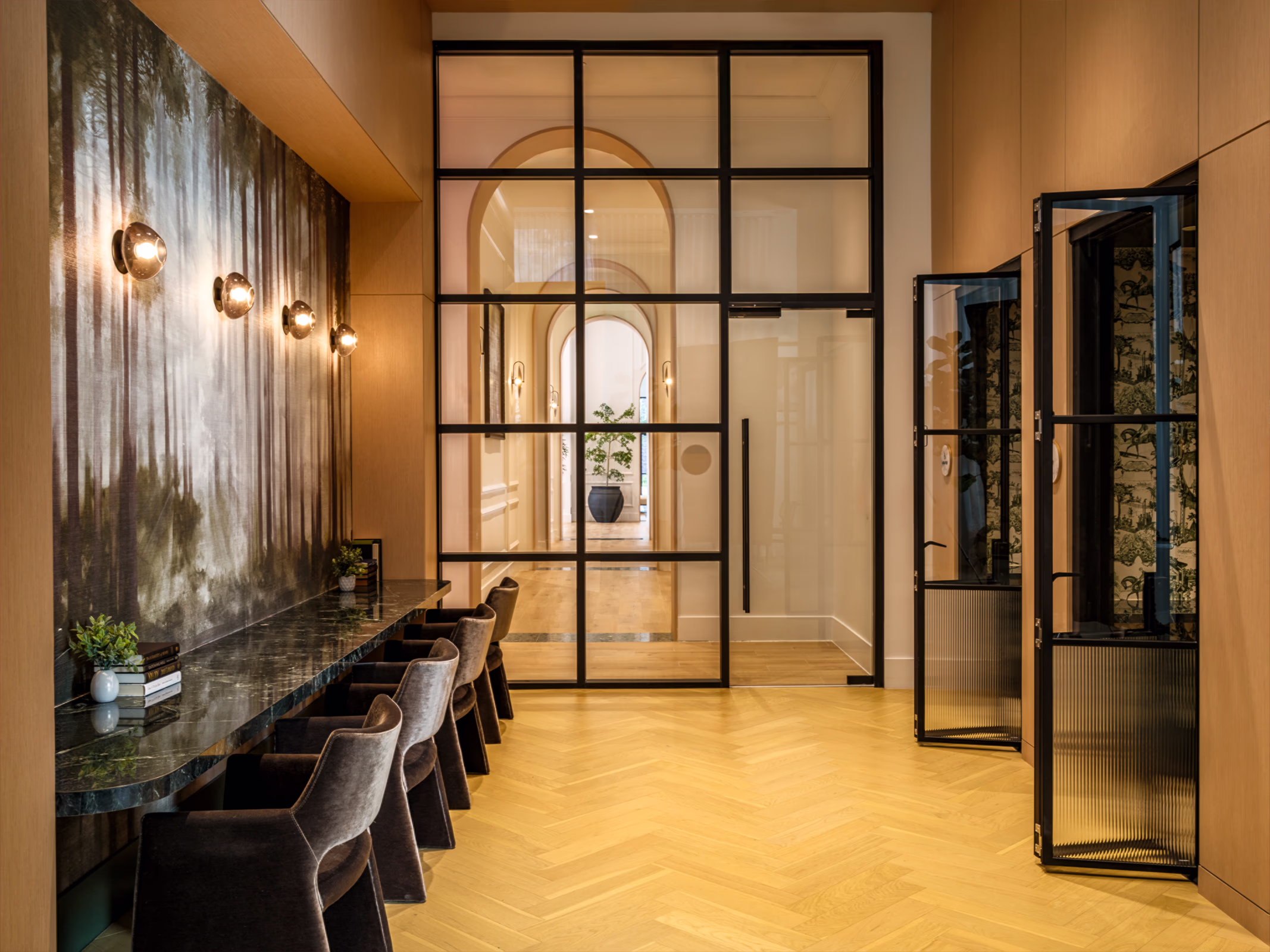 Modera Nations co-working space in Nashville with a marble work bar beneath a misty forest mural, steel-framed glass doors and private work booths.