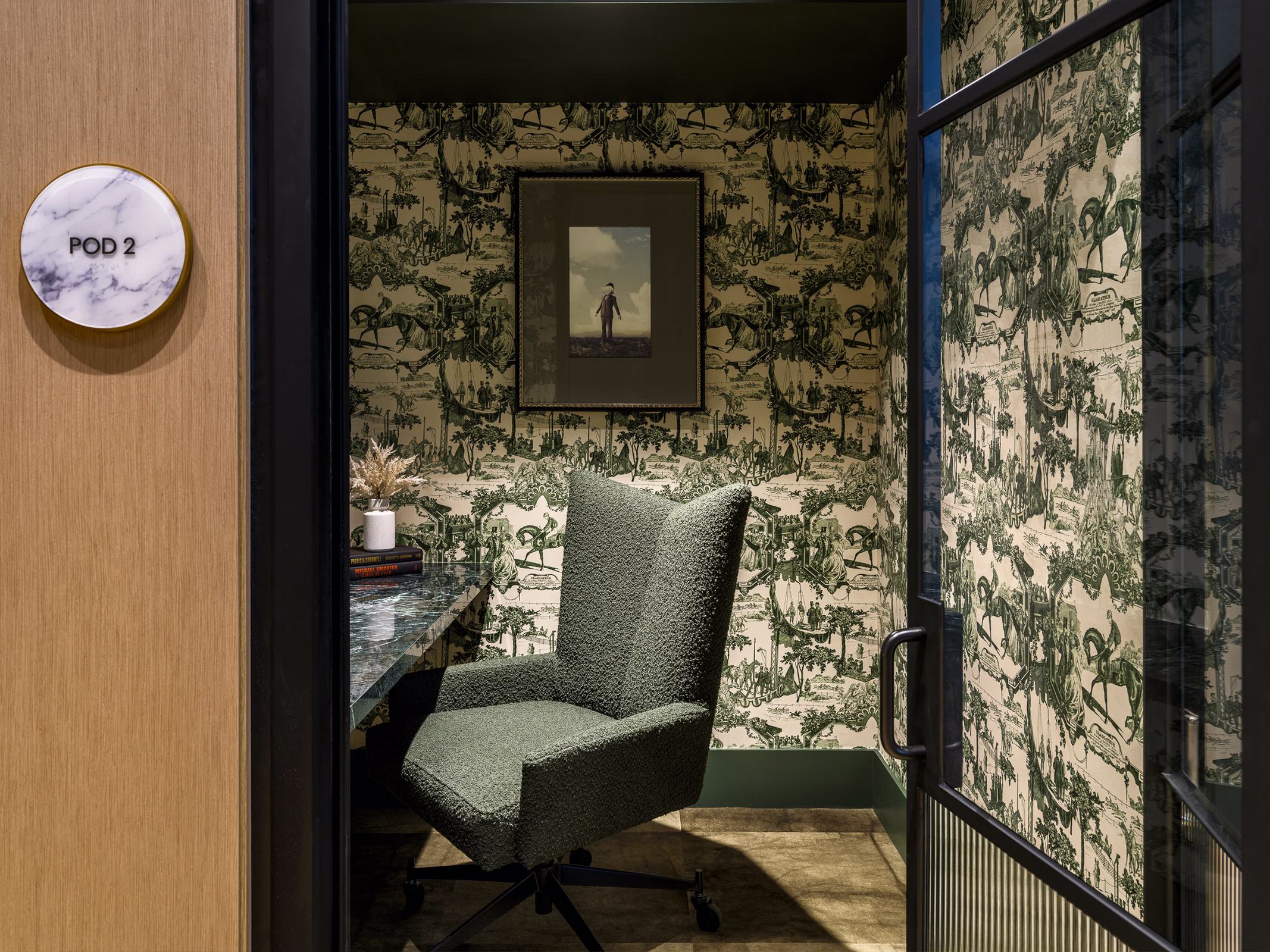 Private work pod at Modera Nations in Nashville with equestrian toile wallpaper, a green boucle desk chair, marble desk and steel-framed glass door.