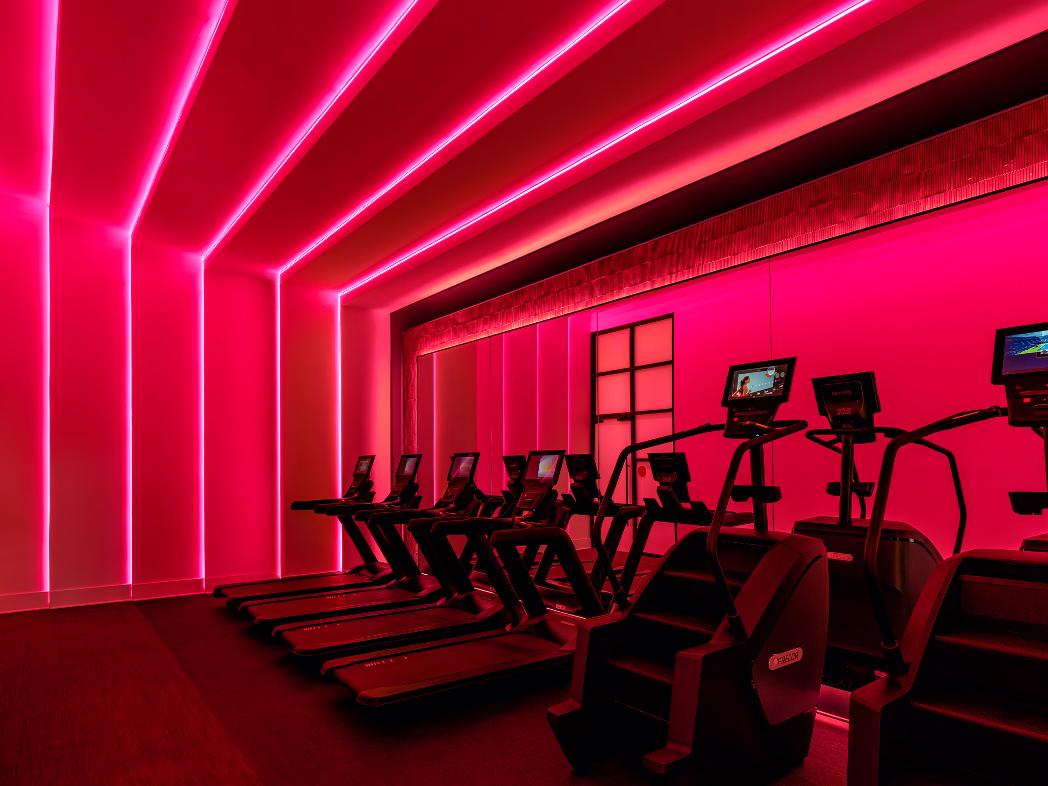 Fitness center cardio room at Modera Nations in Nashville, with treadmills and stair climbers bathed in pink light from LED strips across the walls and ceiling.
