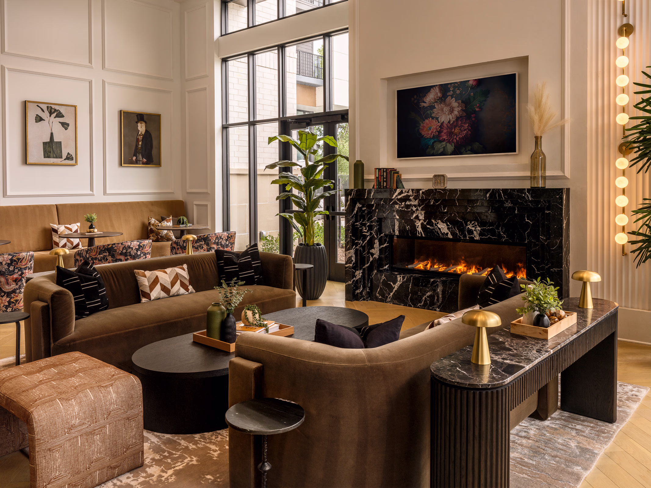 Modera Nations resident lounge in Nashville with velvet sofas around a black marble fireplace, paneled walls, brass lamps and tall steel-framed windows.