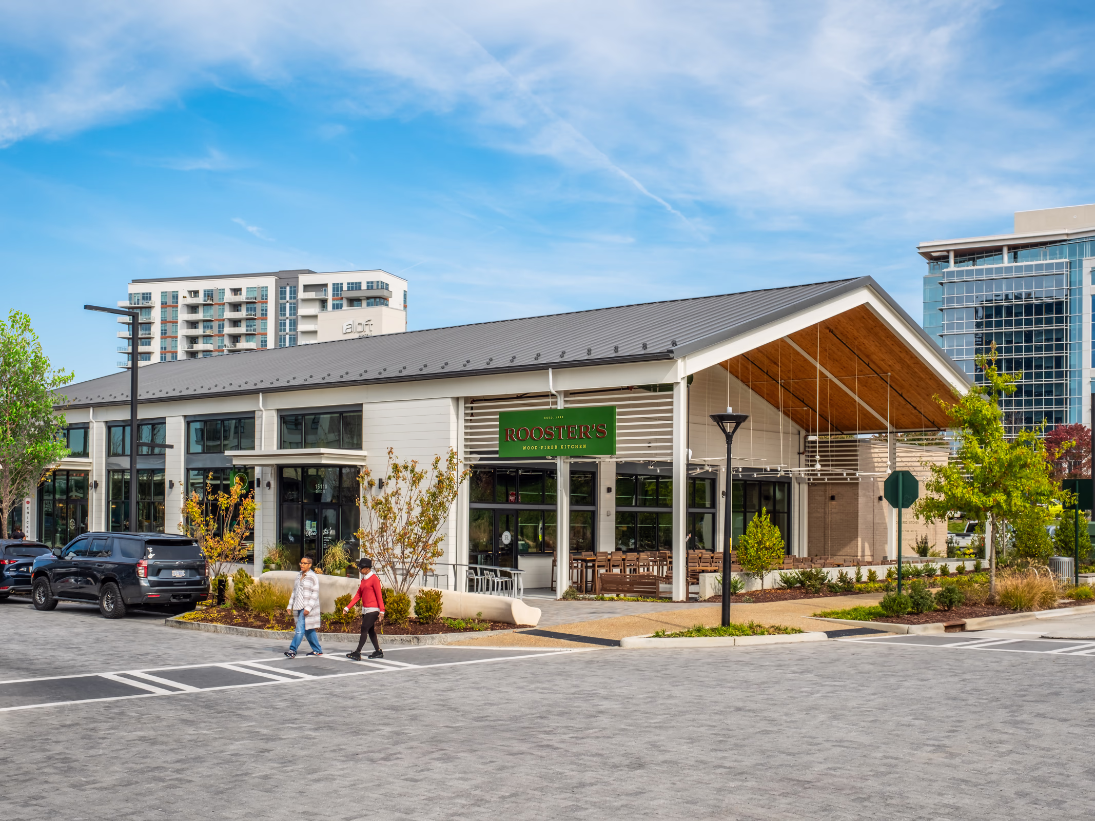 Rooster's Wood-Fired Kitchen at The Bowl at Ballantyne in Charlotte, a white retail building with a metal gable roof, timber-lined canopy and patio.