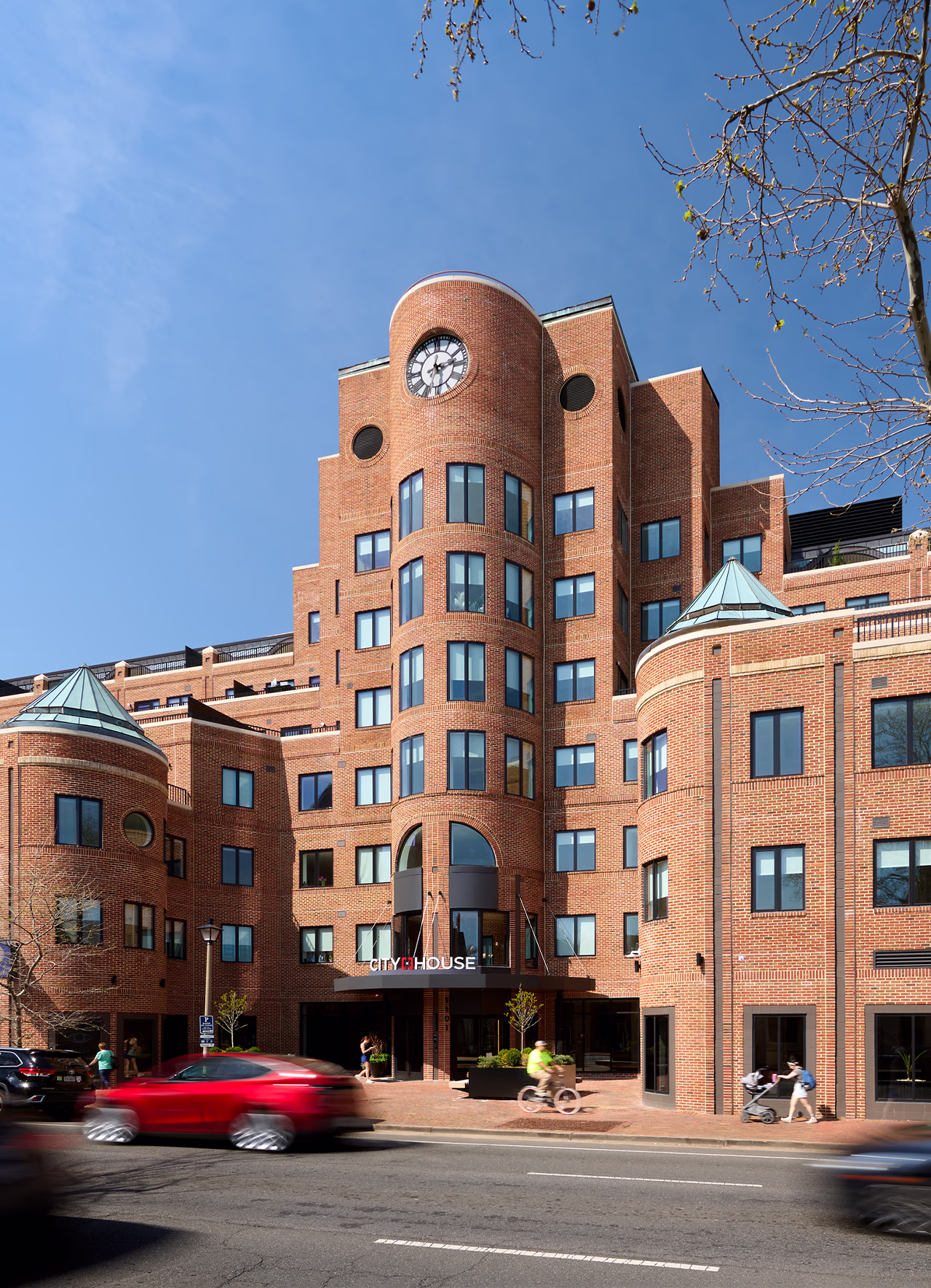 Street view of CityHouse Old Town's central clock tower entrance in Alexandria, Virginia, showing the building's signature curved brick facade, twin turret towers, and King Street entry with CityHouse signage.