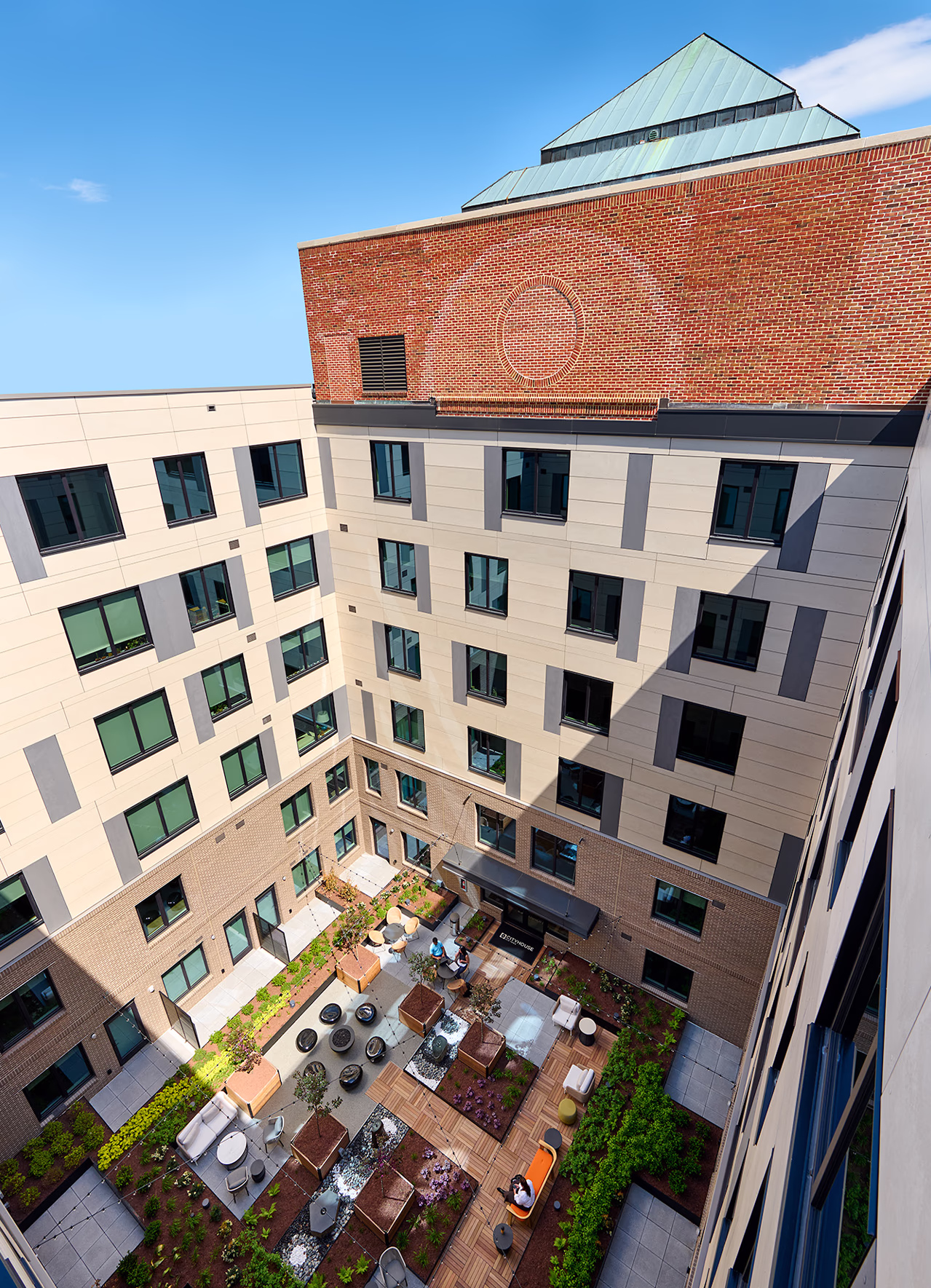 Aerial view looking down into CityHouse Old Town's landscaped courtyard in Alexandria, Virginia, showing seating areas, water features, wood decking, and residential windows lining the surrounding facades.