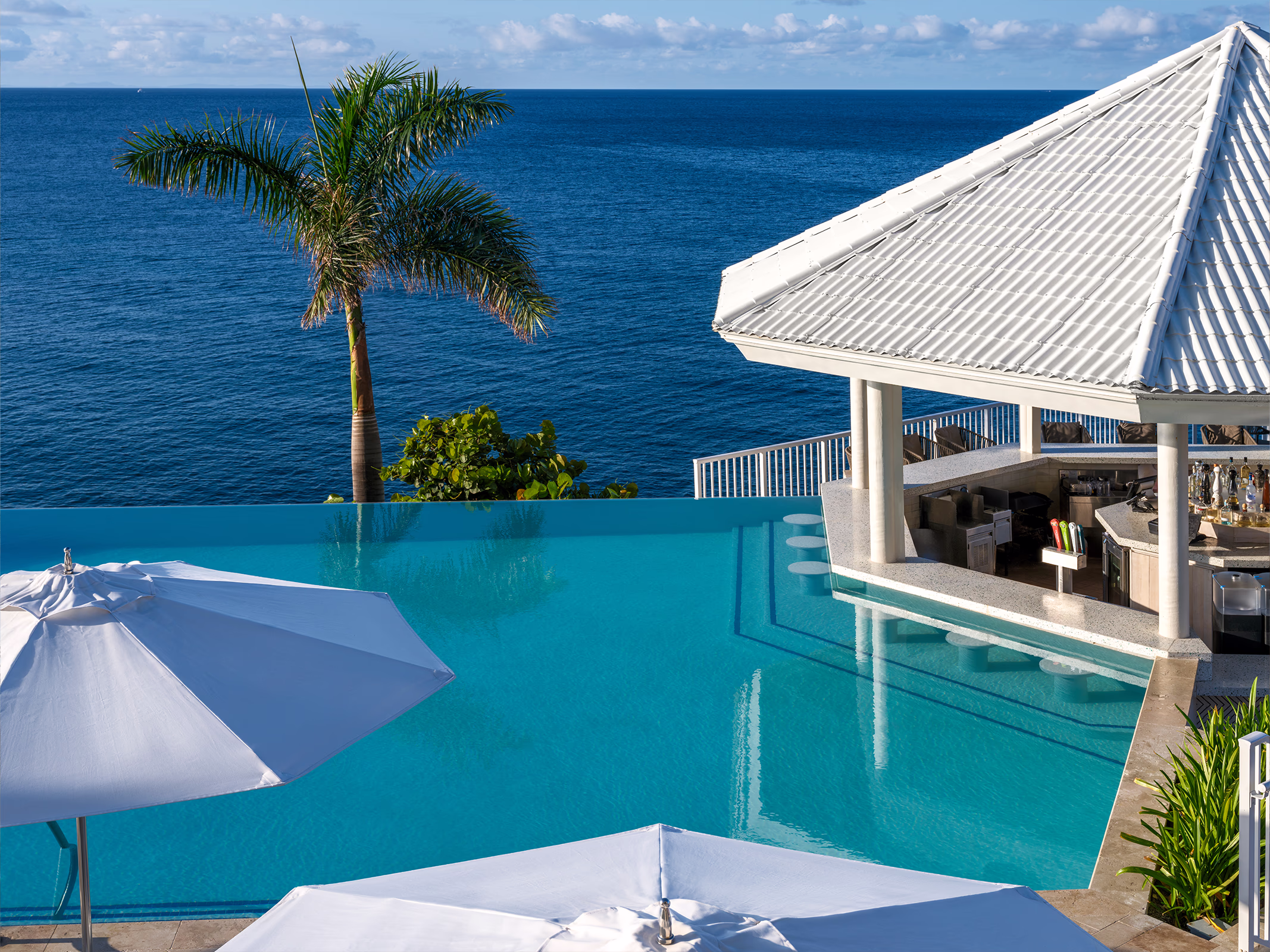 Swim-up infinity pool bar at The Edge Bar, Frenchman's Reef, overlooking the Caribbean Sea with palm trees and white umbrellas.