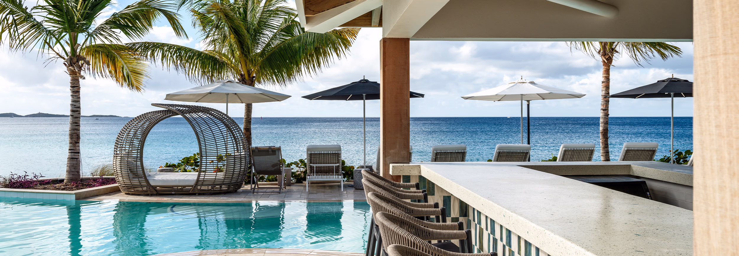 Tide Pool at Buoy Haus, Frenchman's Reef, with a woven cabana daybed, poolside bar, and ocean views framed by palm trees.