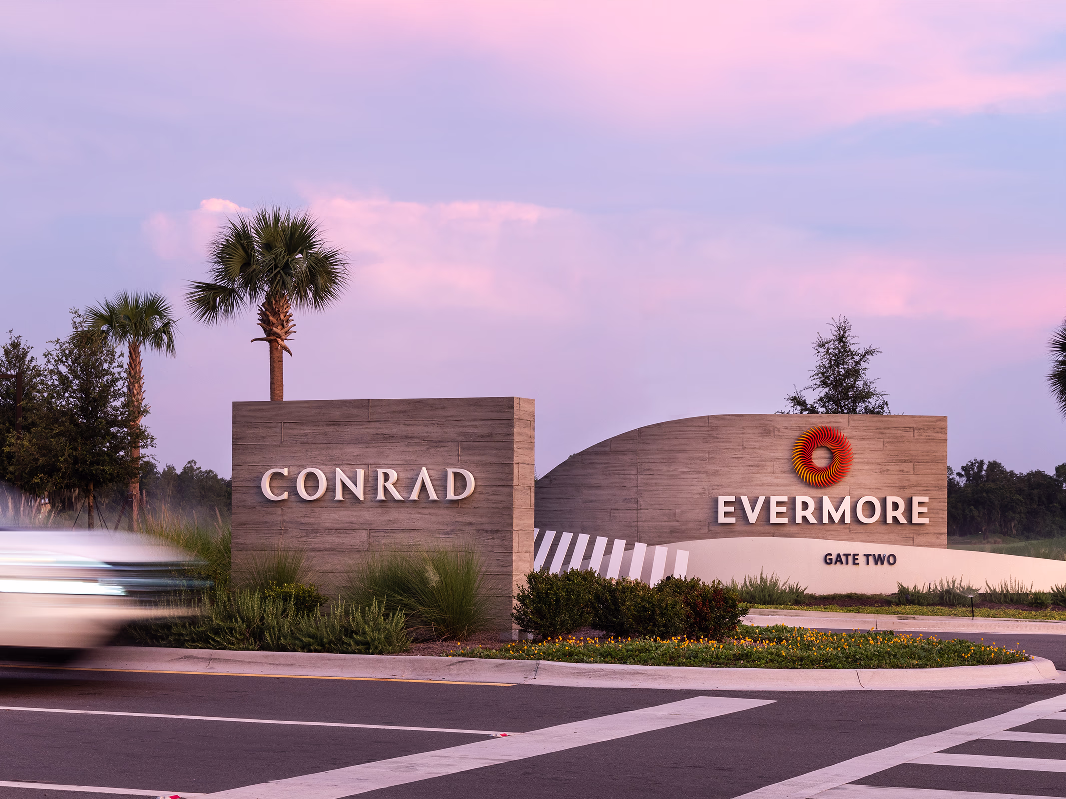 Board-formed concrete monument signs for Conrad Orlando and Evermore Gate Two at the resort roadway entrance under a pink and purple sunset sky.