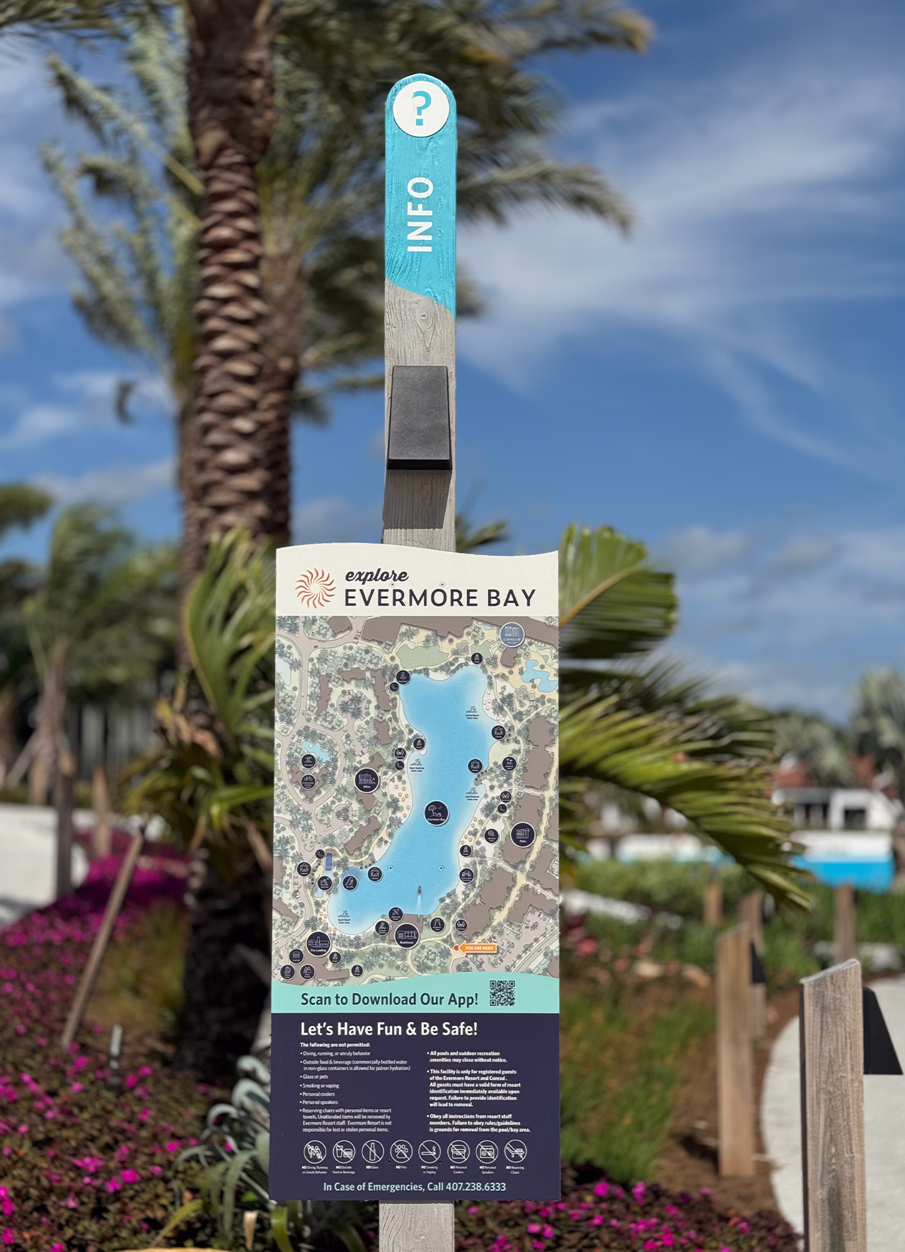 Timber post info sign at Evermore Orlando Resort showing an illustrated Evermore Bay lagoon map, app QR code and pool safety rules beside palms.