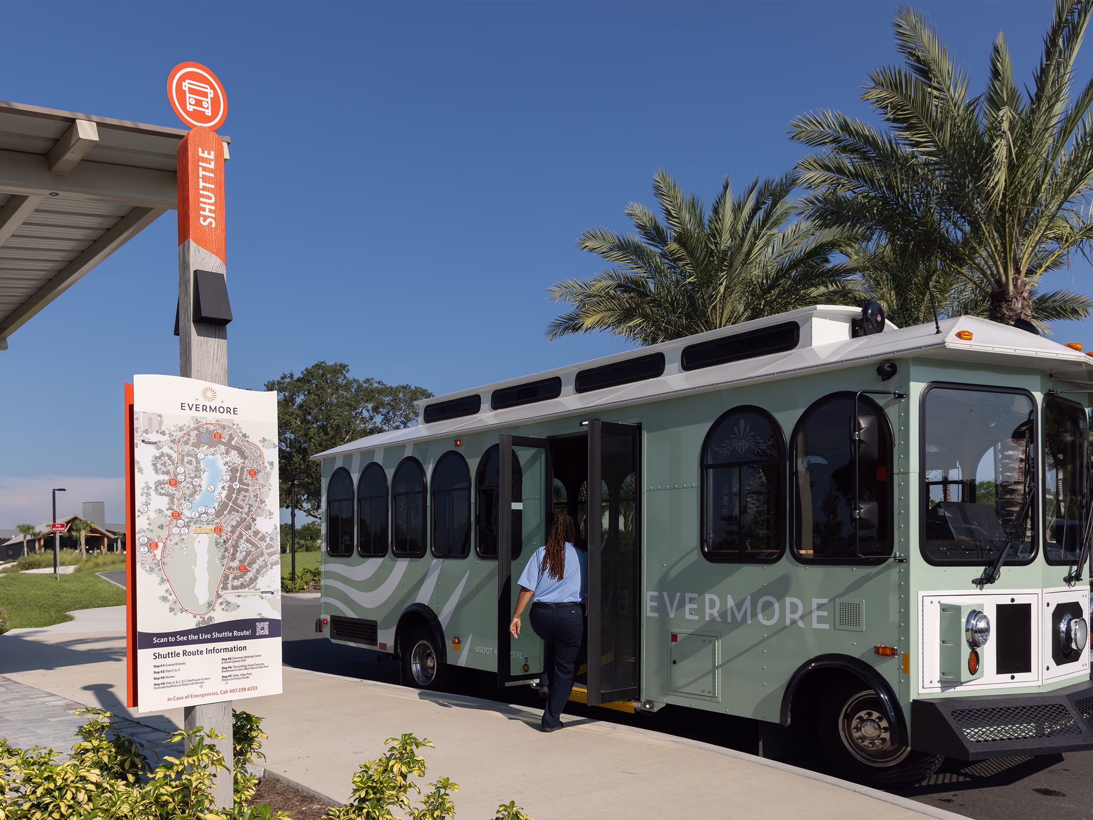 Orange shuttle stop marker and route map sign at Evermore Orlando Resort as a guest boards the mint green Evermore trolley beneath palm trees.