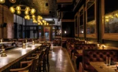 Interior view from the bar at The Kennedy looking toward the entrance with warm lighting, custom seating, and large street-facing windows