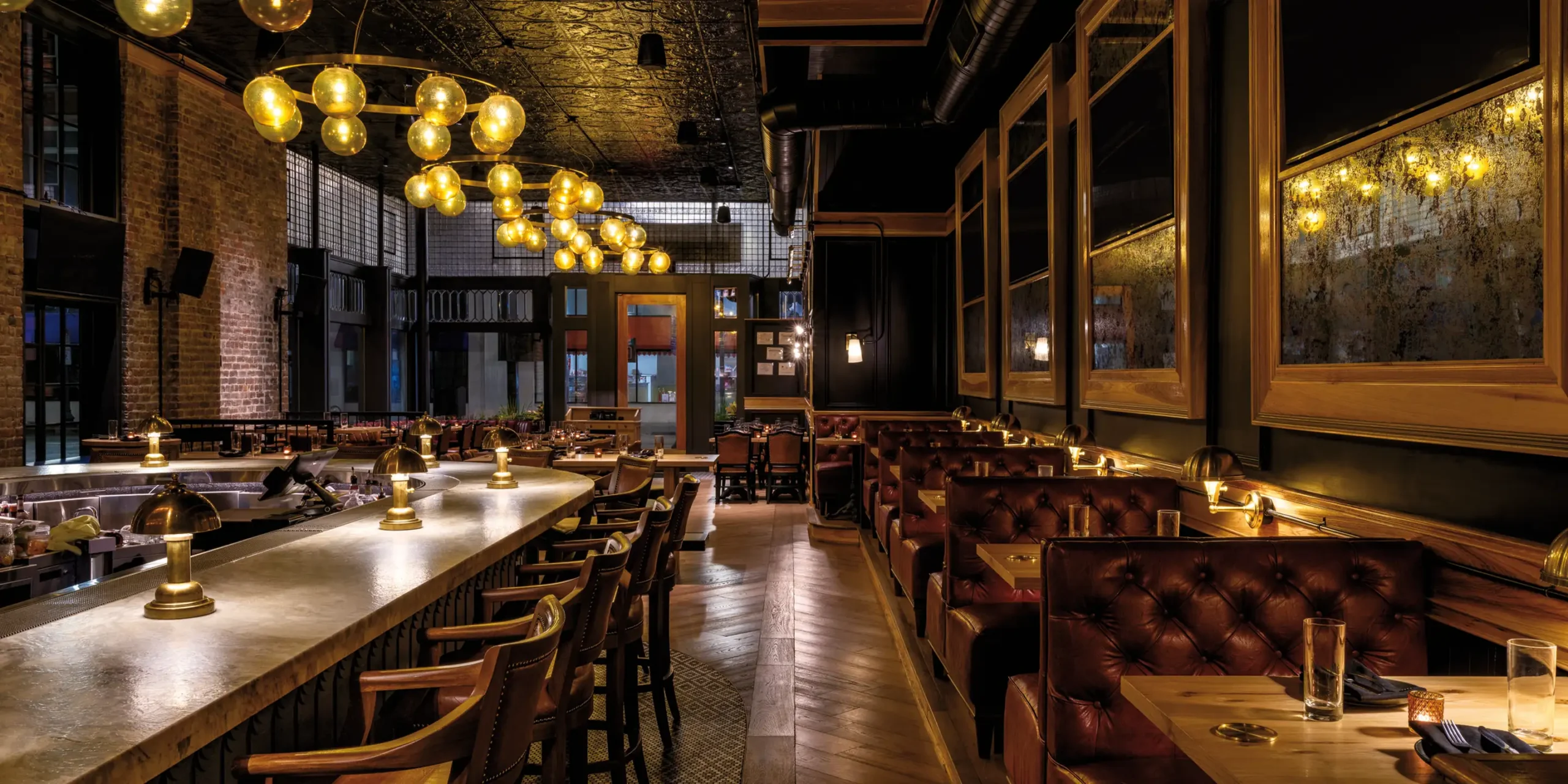 Interior view from the bar at The Kennedy looking toward the entrance with warm lighting, custom seating, and large street-facing windows