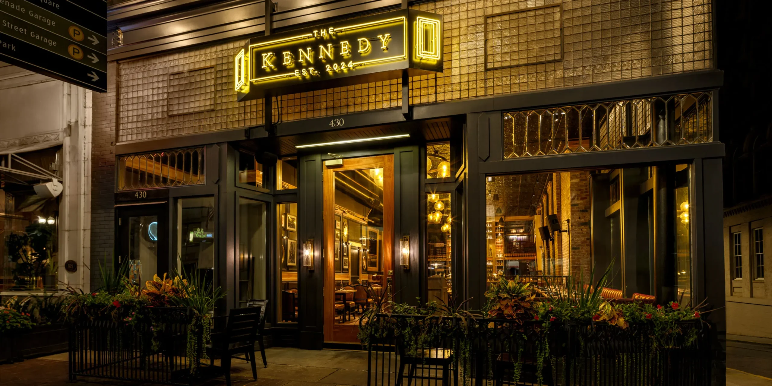 Exterior of The Kennedy gastropub with neon signage, dark blue trim, and glowing interior visible from the street