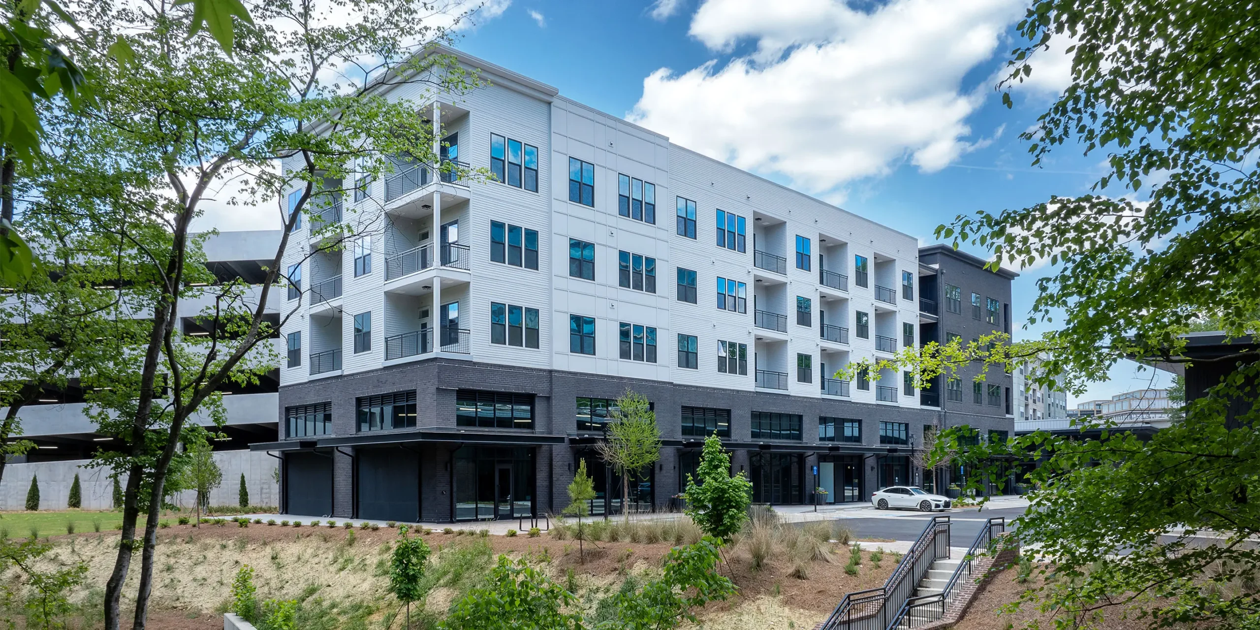 Exterior view of a residential building at AMLI Brookhaven from adjacent trail, featuring dark brick base and white upper stories.