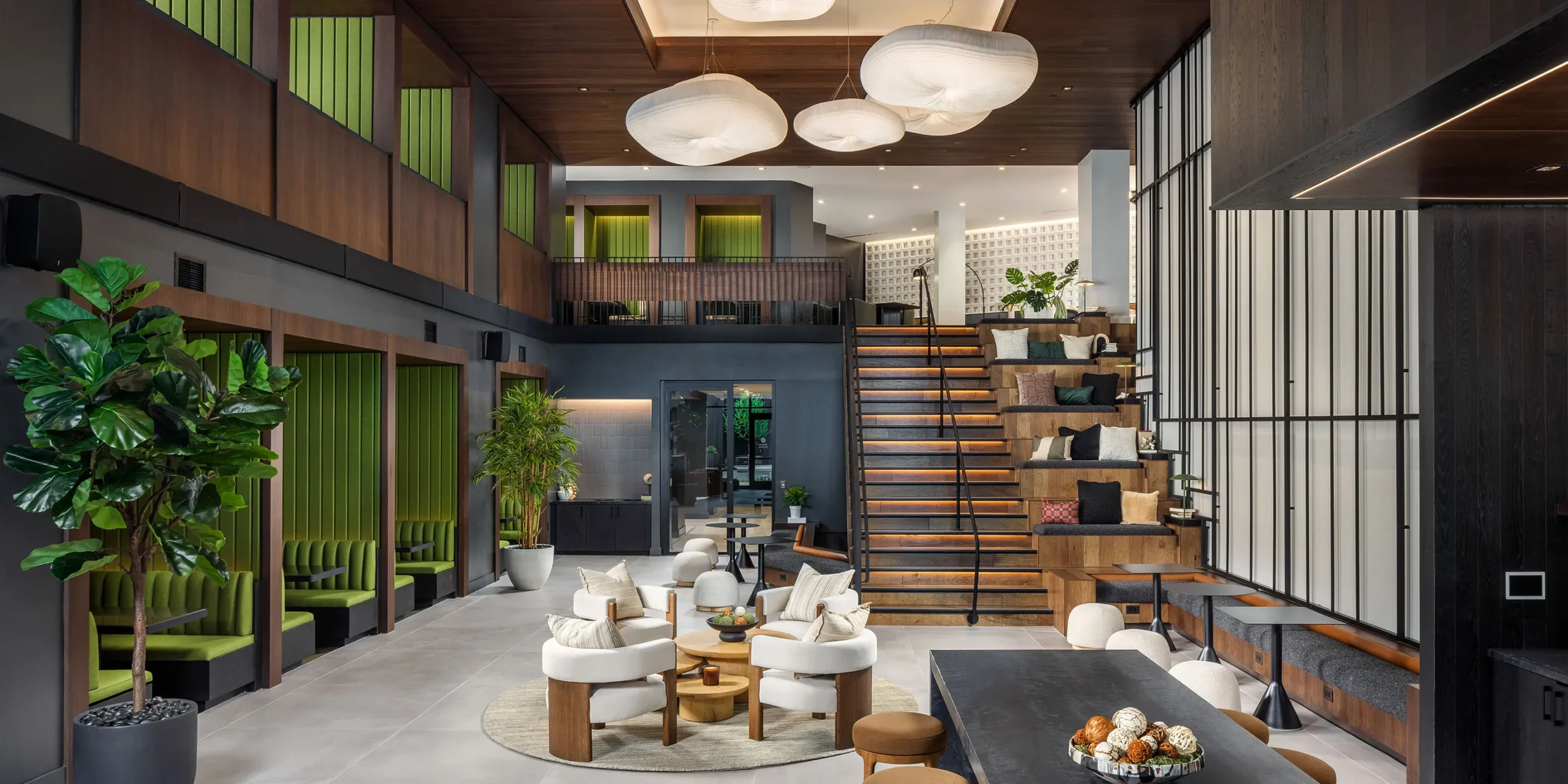 Double-height lounge with cloud-like lighting, green velvet seating, and open stair access to upper level.