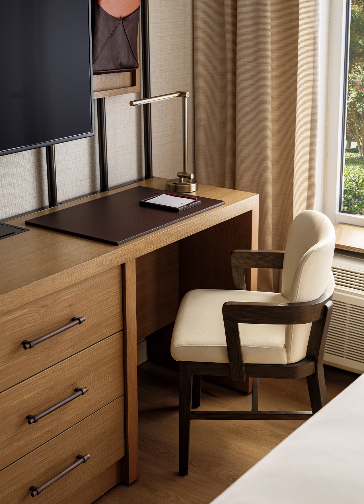 Built-in desk nook at The James F. Martin Inn with a cream armchair, brass desk lamp, and leather desk pad beside a curtained window.