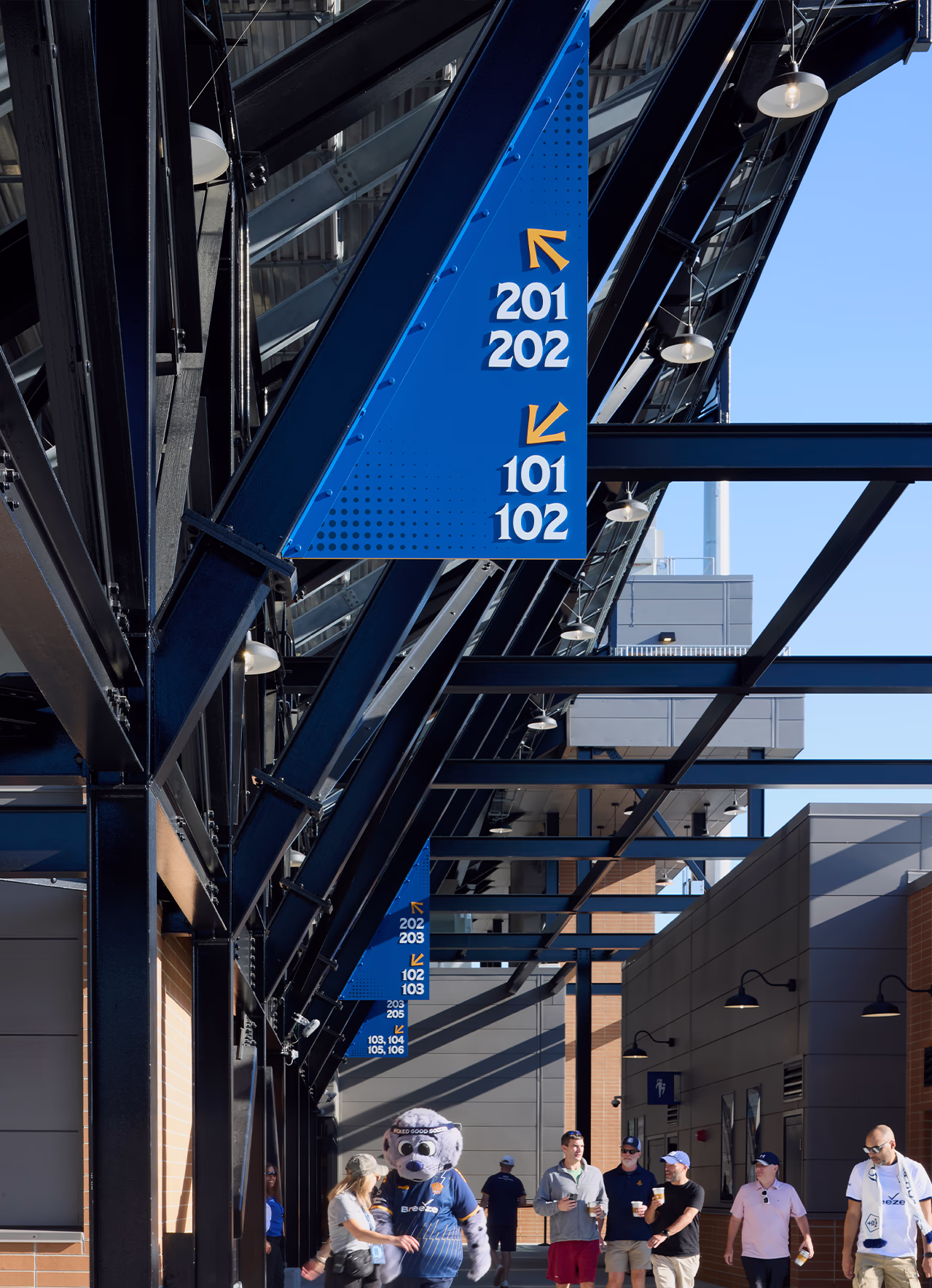 Blue blade signs with section numbers and yellow arrows hang from exposed steel along the concourse at Centreville Bank Stadium, directing fans to their seats.