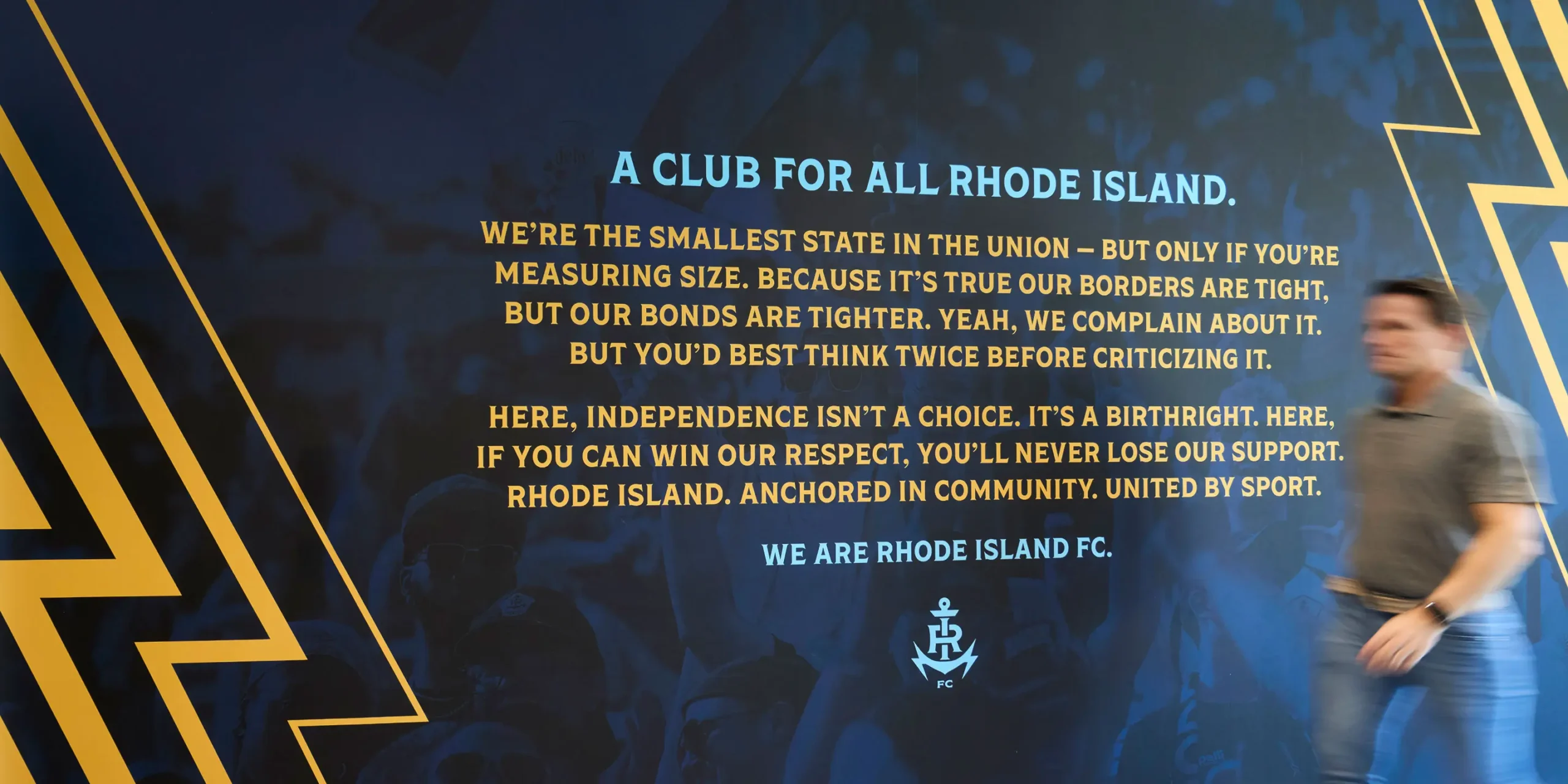 Interior wall graphic featuring Rhode Island FC branding and an inspirational message celebrating state pride and community identity.