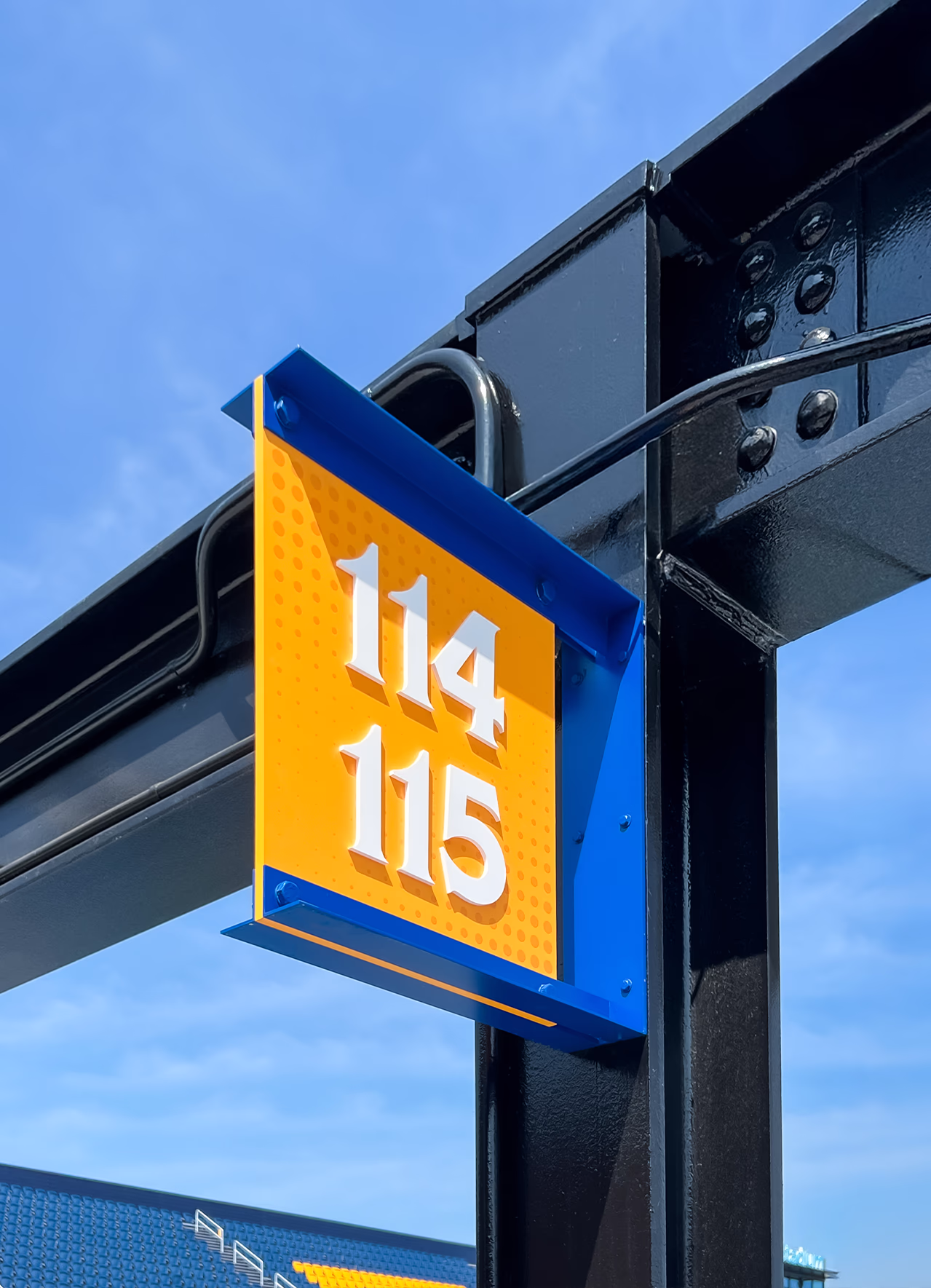 Close-up of a yellow and blue section blade sign for 114 and 115 mounted to an exposed steel column at Centreville Bank Stadium.