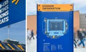 Industrial-style “Stadium Information” sign with map and key alongside overhead pedestrian directional signage; dimensional letters and stadium seating reading “RIFC” visible in background.
