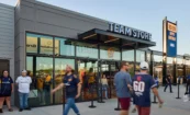 “Team Store” open-face channel letters with neon illumination mounted above the entrance canopy, with vinyl team graphics applied to the glass facade.