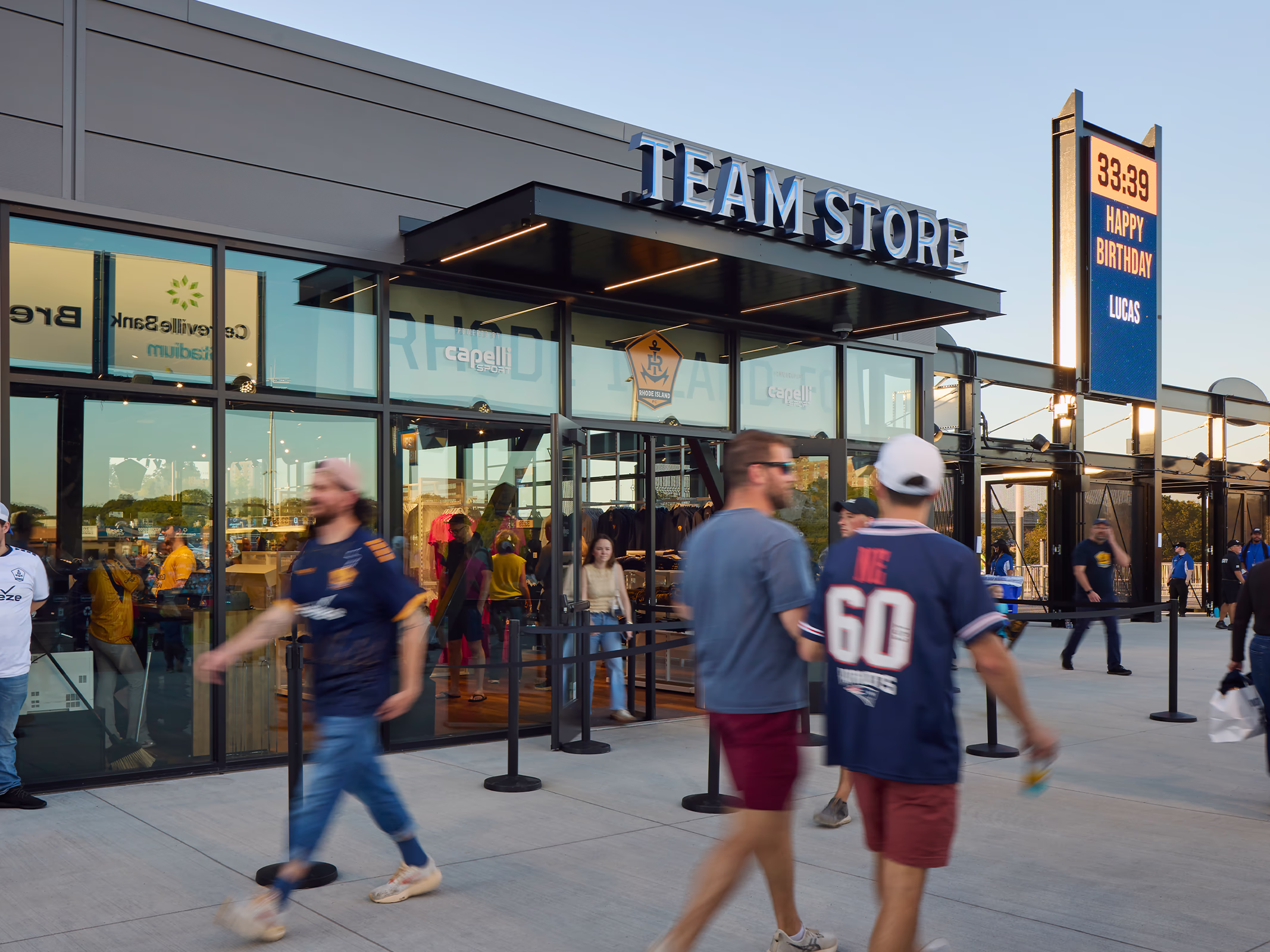 Dimensional Team Store signage marks the Rhode Island FC retail storefront at Centreville Bank Stadium as fans pass on the concourse at dusk.
