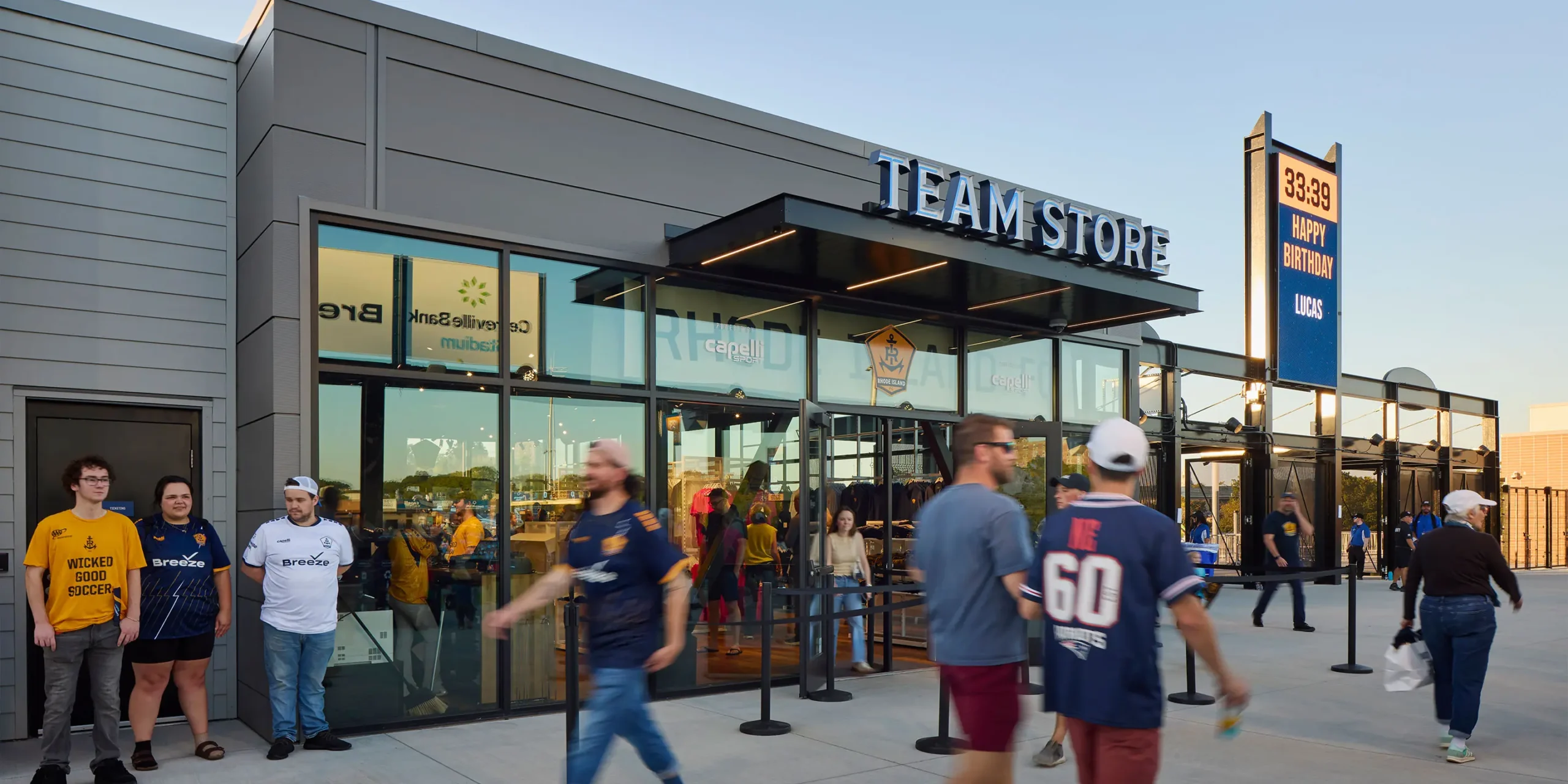“Team Store” open-face channel letters with neon illumination mounted above the entrance canopy, with vinyl team graphics applied to the glass facade.