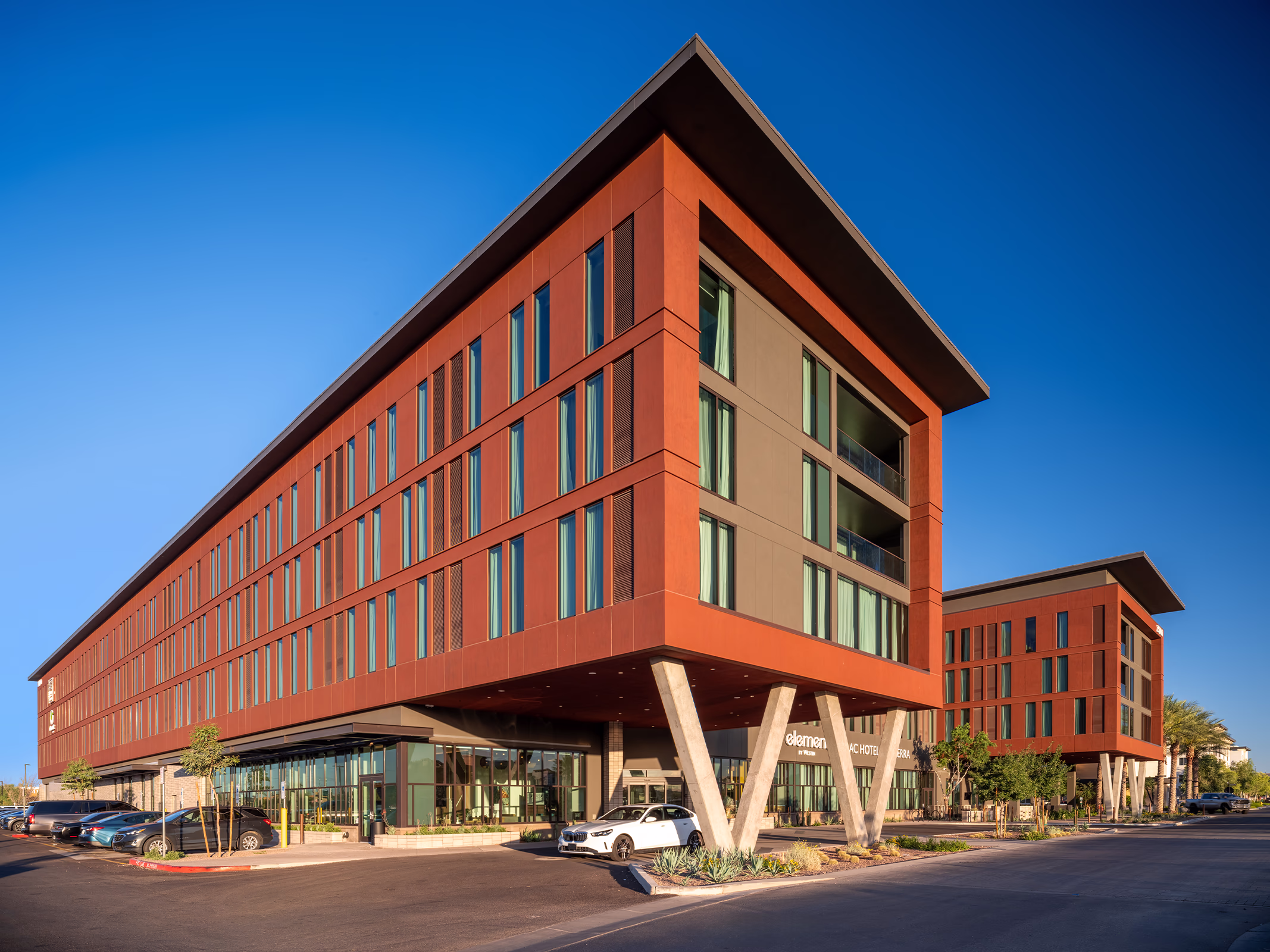 Wide daytime exterior view of the dual-brand AC Hotel and Element by Westin in Norterra, showing the cantilevered corner supported by angled V-shaped columns and street-level entrance