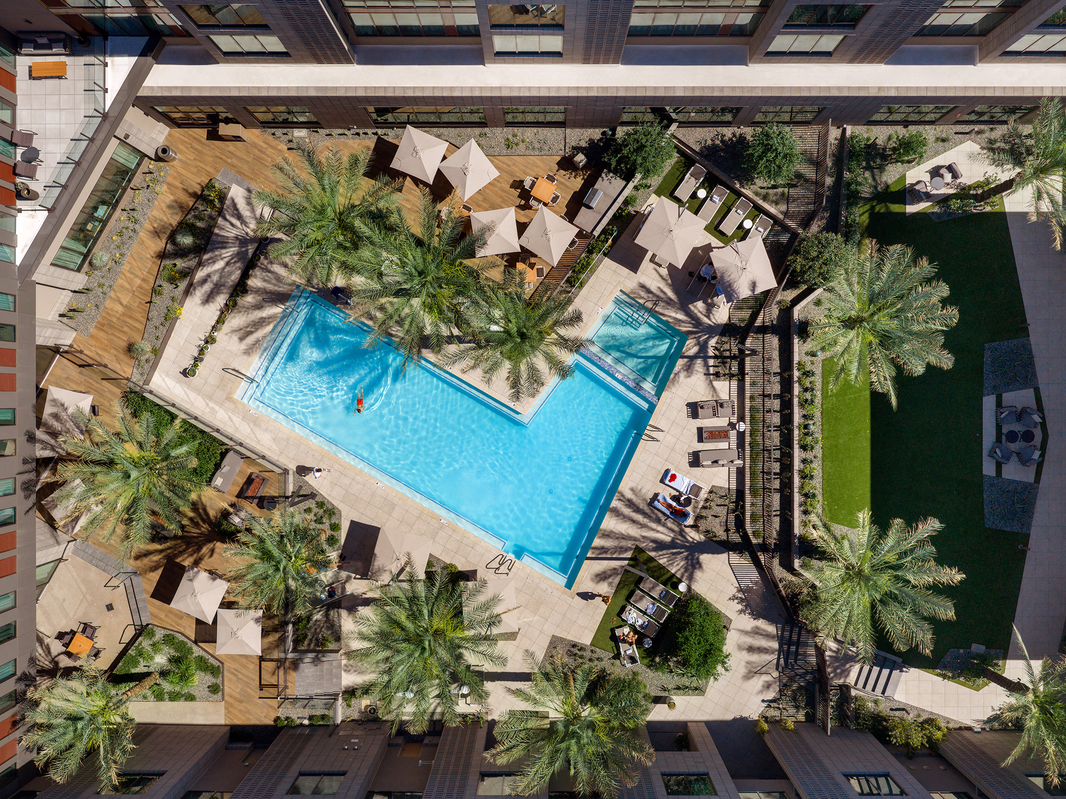 Aerial view of the resort courtyard at the Norterra hotel, showing the L-shaped pool, spa, shaded lounge areas, and adjacent event lawn surrounded by palm trees