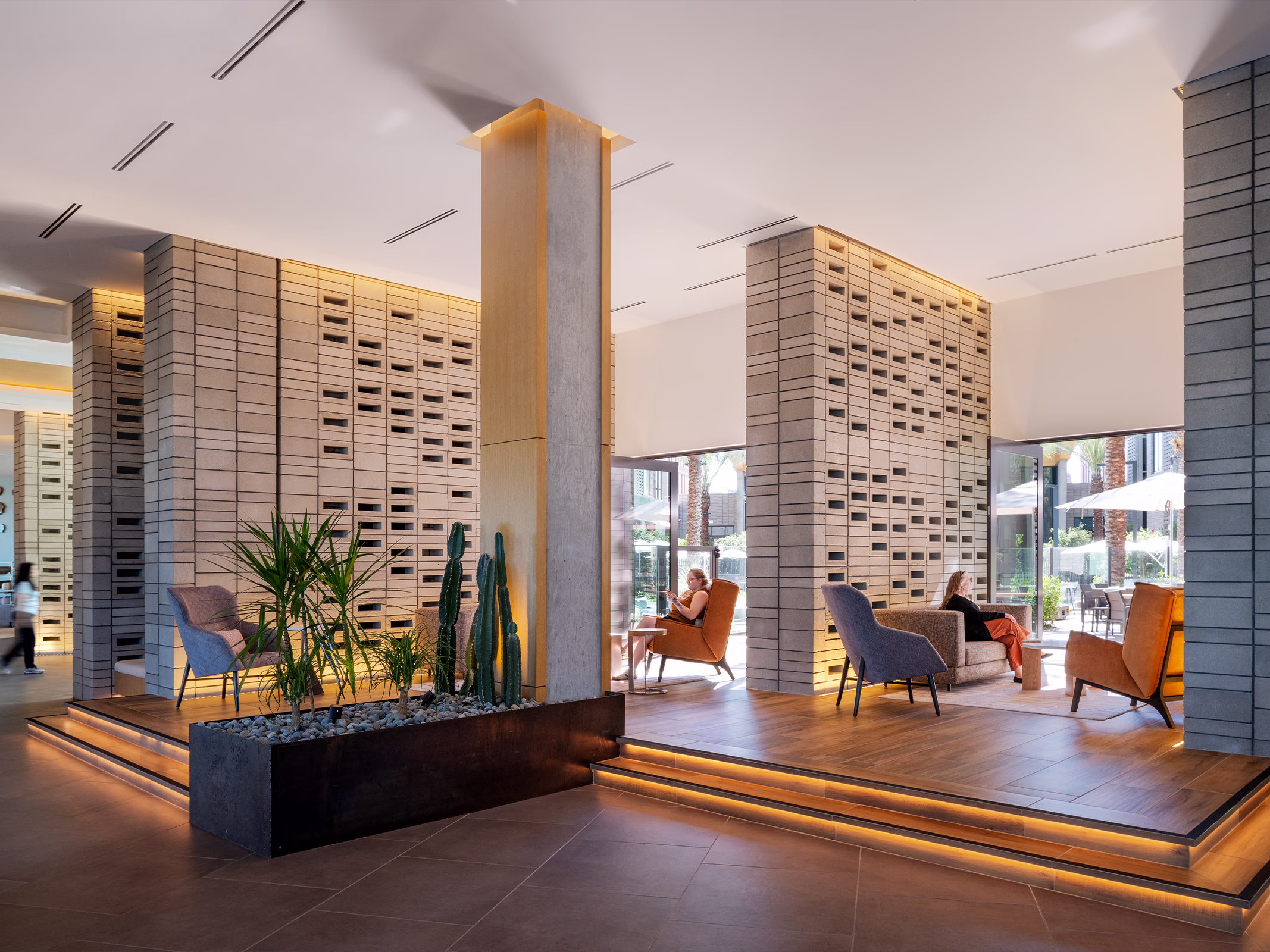 Interior lounge seating area at the Norterra hotel with textured perforated stone columns, desert planting, and glass doors opening to the courtyard
