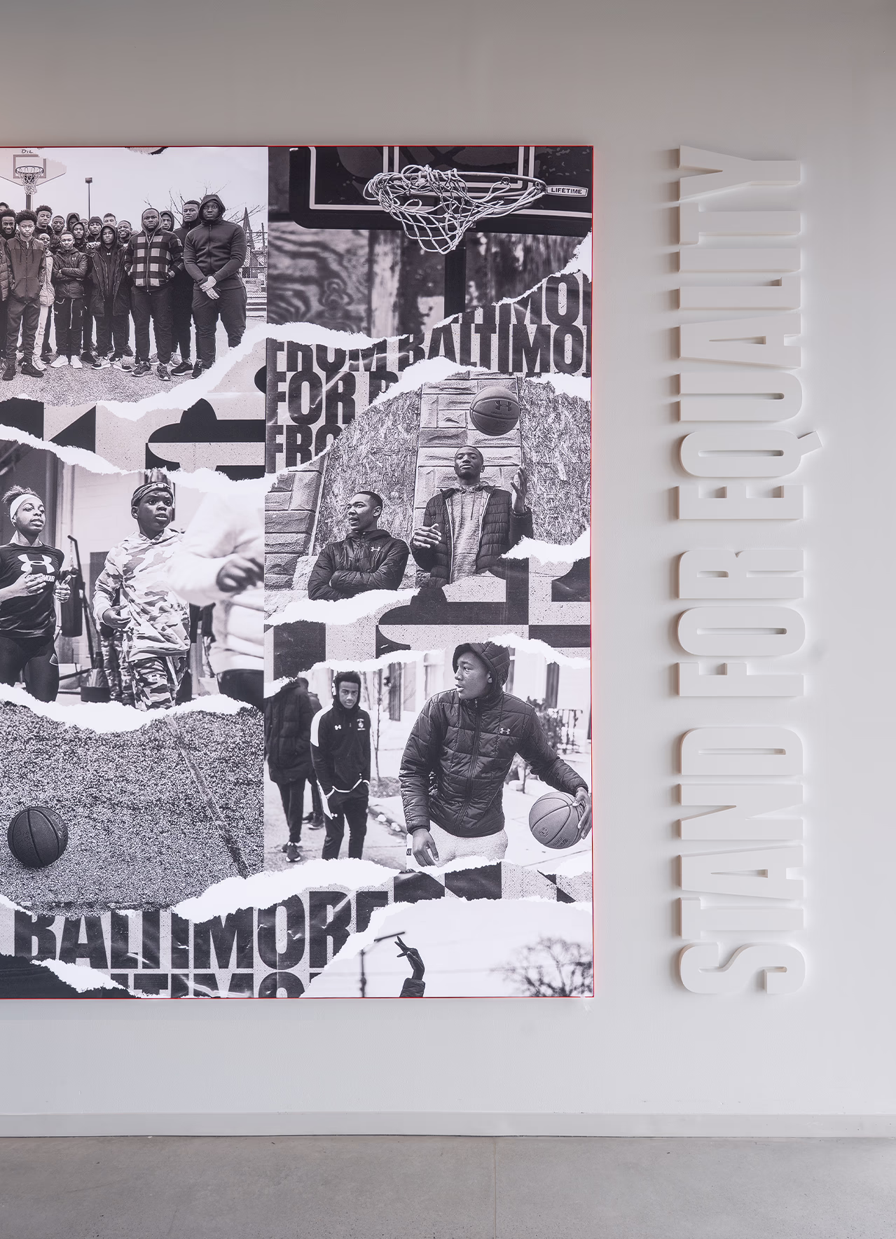 Close-up of a black-and-white photo collage wall at Under Armour headquarters celebrating Baltimore basketball culture, alongside dimensional 'Stand for Equality' lettering on the adjacent wall.