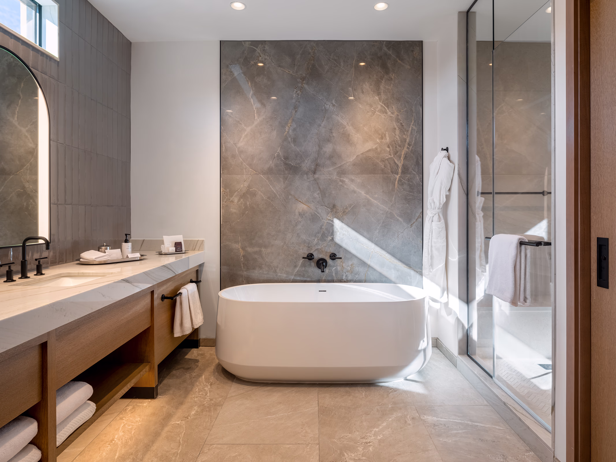 Spa-style bathroom in a Villas at Canyon Suites residence with a freestanding soaking tub, marble accent wall, and glass-enclosed shower.