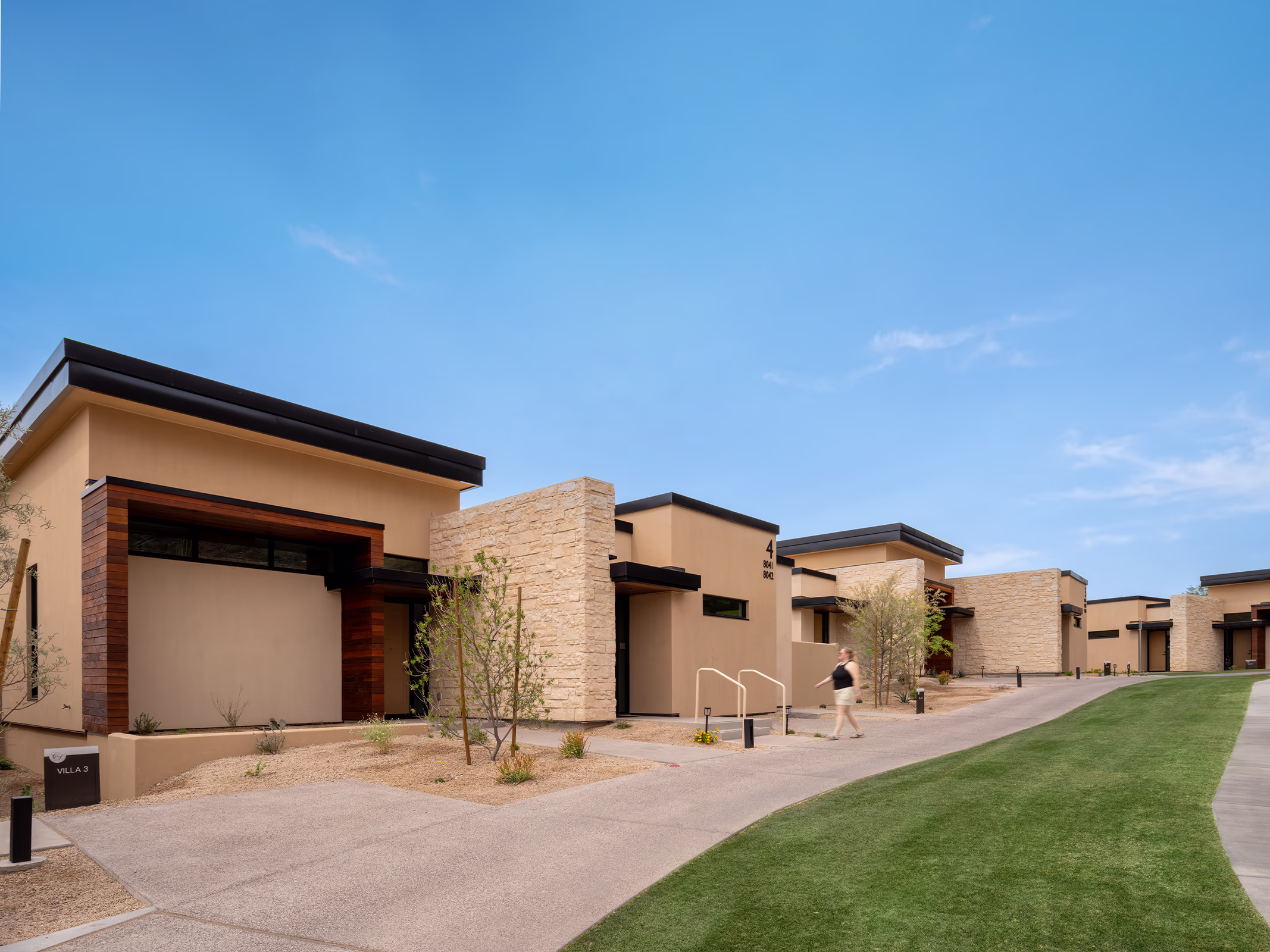 Exterior of a Villas at Canyon Suites residence showing stone and stucco facades, wood accents, and desert landscaping along the pedestrian walkway.
