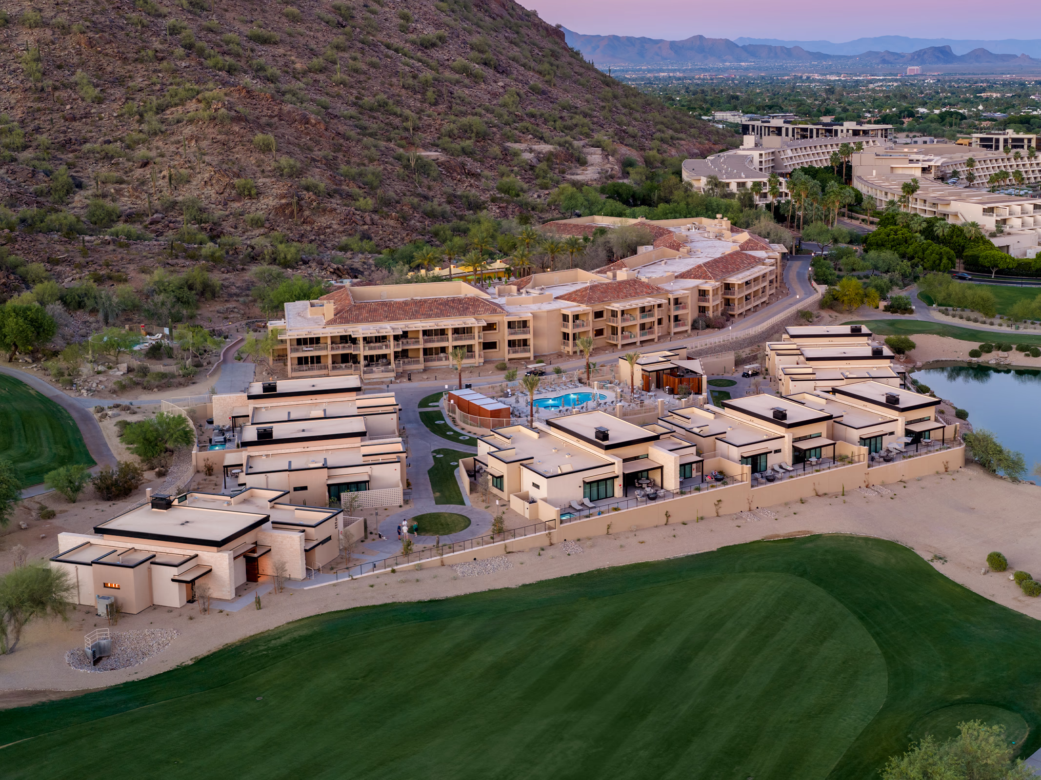 Aerial view of The Villas at Canyon Suites at the base of Camelback Mountain, showing the private pool, villa rooftops, and golf course at dusk.
