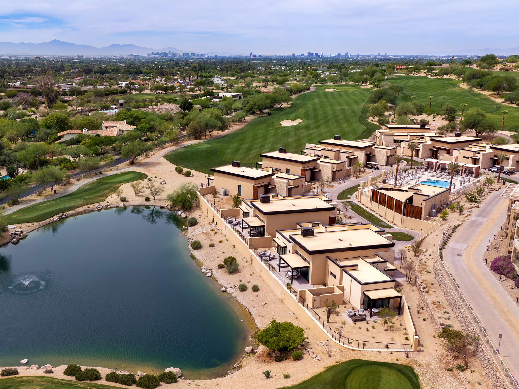 Daytime aerial view of The Villas at Canyon Suites along the golf course and lake, with the Phoenix skyline visible on the horizon.