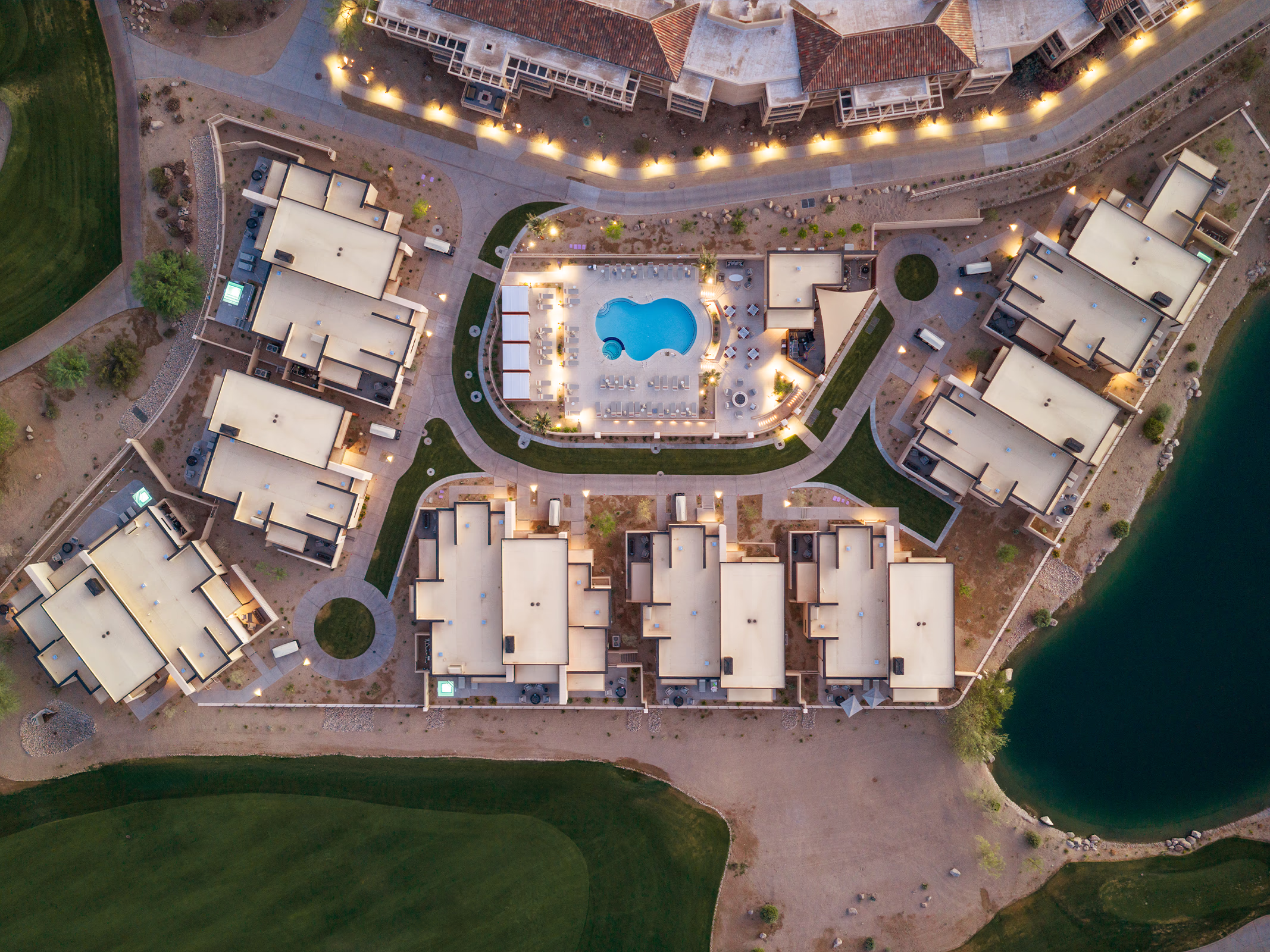Overhead view of The Villas at Canyon Suites showing the private pool courtyard and villa rooftops illuminated at dusk beside the golf course and lake.