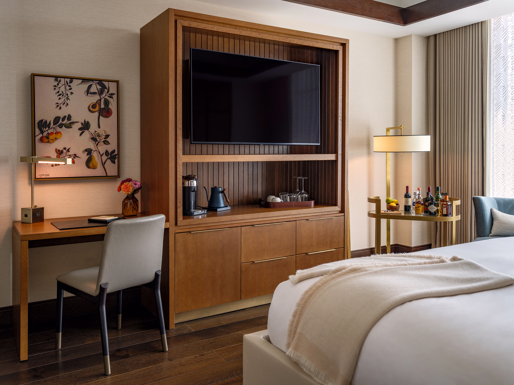 Guestroom workspace at The Laurel Hotel & Spa at Auburn University, with a wood desk, wall-mounted TV, coffee station, and a bar cart stocked with spirits.