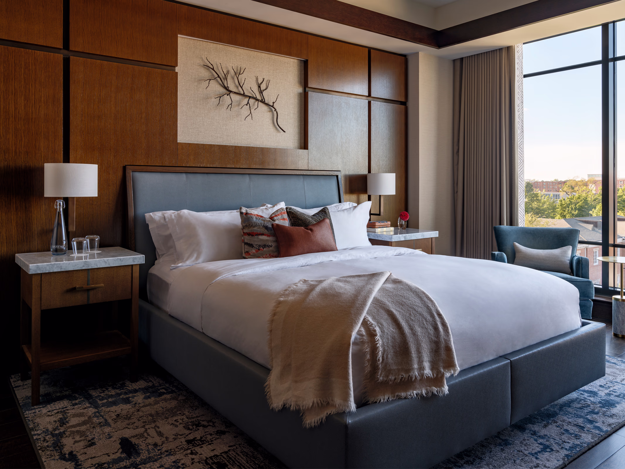 King guestroom at The Laurel Hotel & Spa at Auburn University, with a leather bed, walnut wall paneling, branch wall art, and a city view.