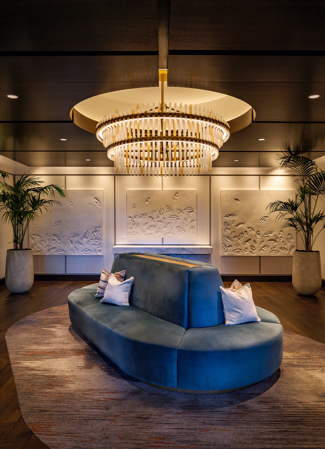 Lobby lounge at The Laurel Hotel & Spa at Auburn University, with a curved blue velvet sofa, tiered brass chandelier, and botanical relief wall panels.