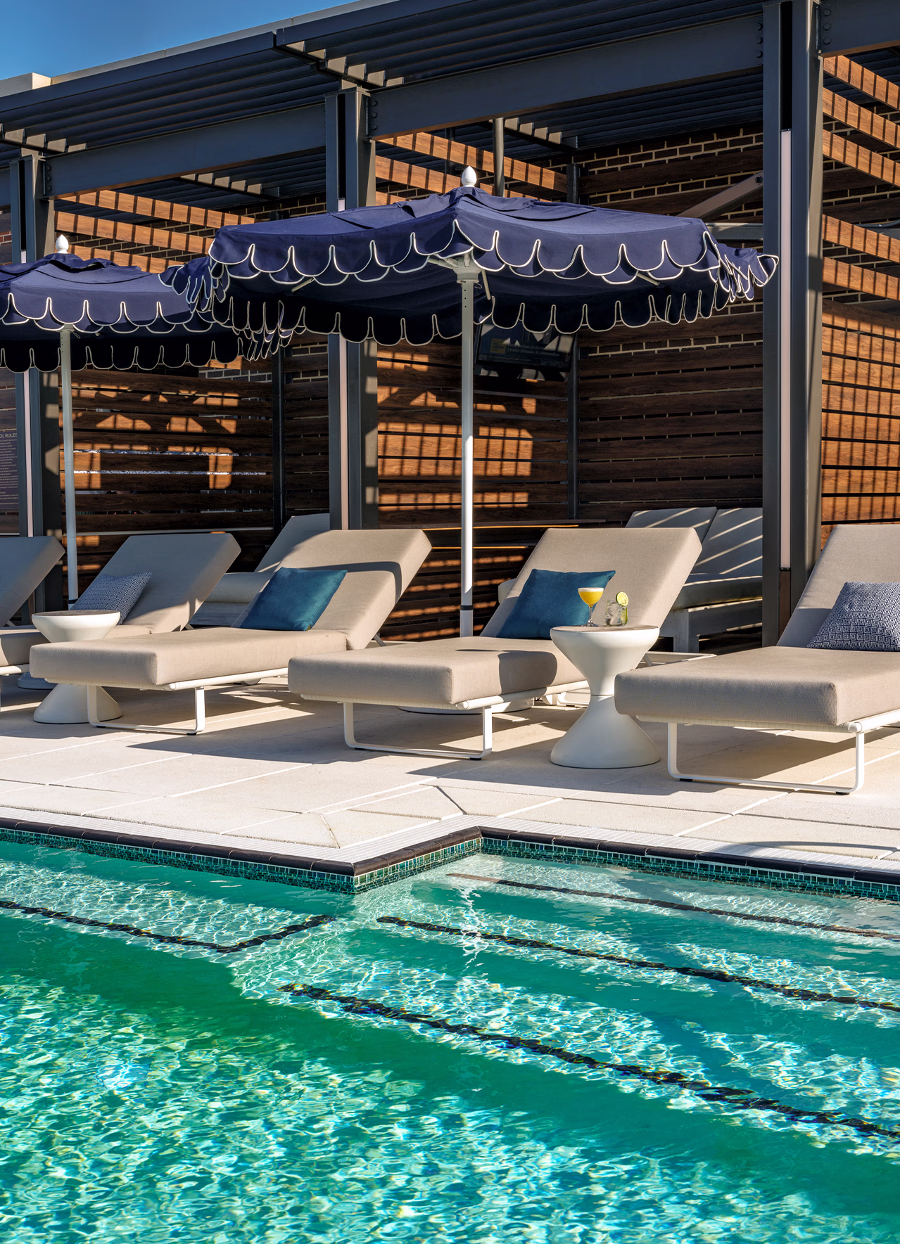 Rooftop lap pool at The Laurel Hotel & Spa at Auburn University, with scalloped navy umbrellas, lounge chairs, and a cocktail on a poolside table.